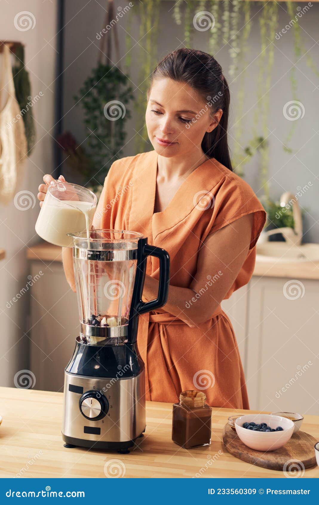 Woman in orange dress pouring fresh milk into electric blender Stock Photo  by Pressmaster