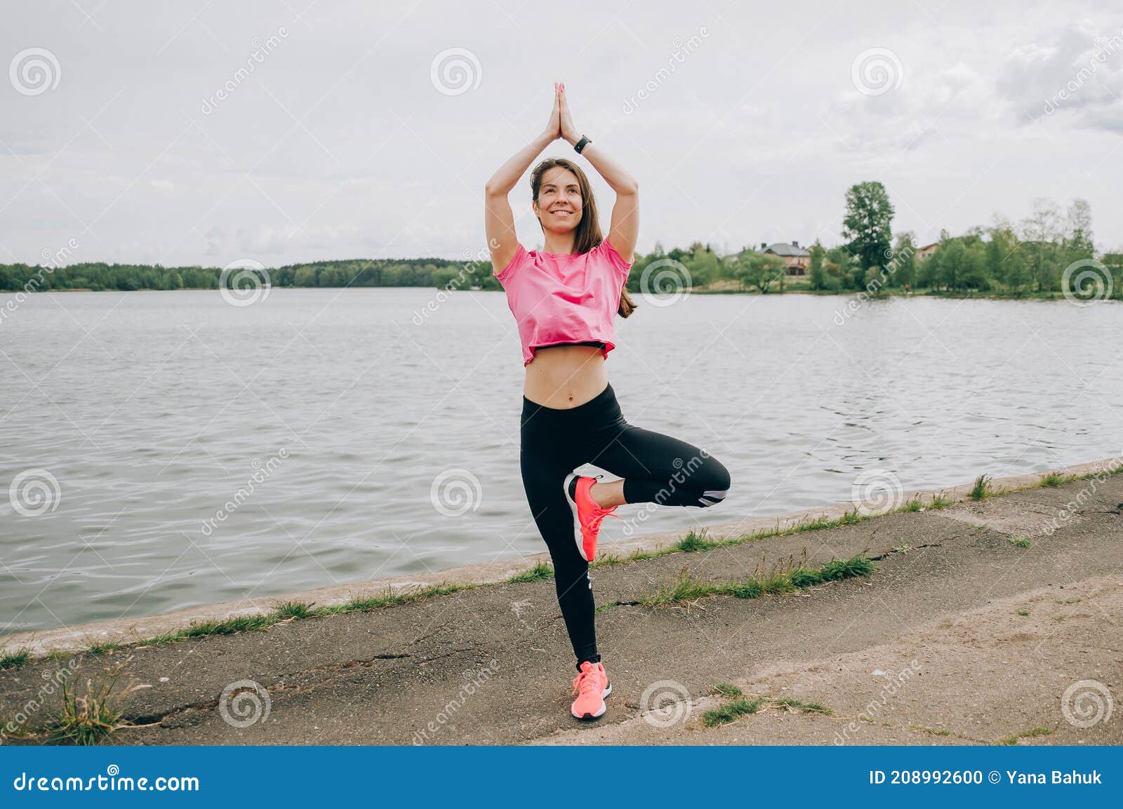 young brunette woman with bare feet  wearing black and purple fitness outfit  stretching on violet yoga mat outside on wooden pier