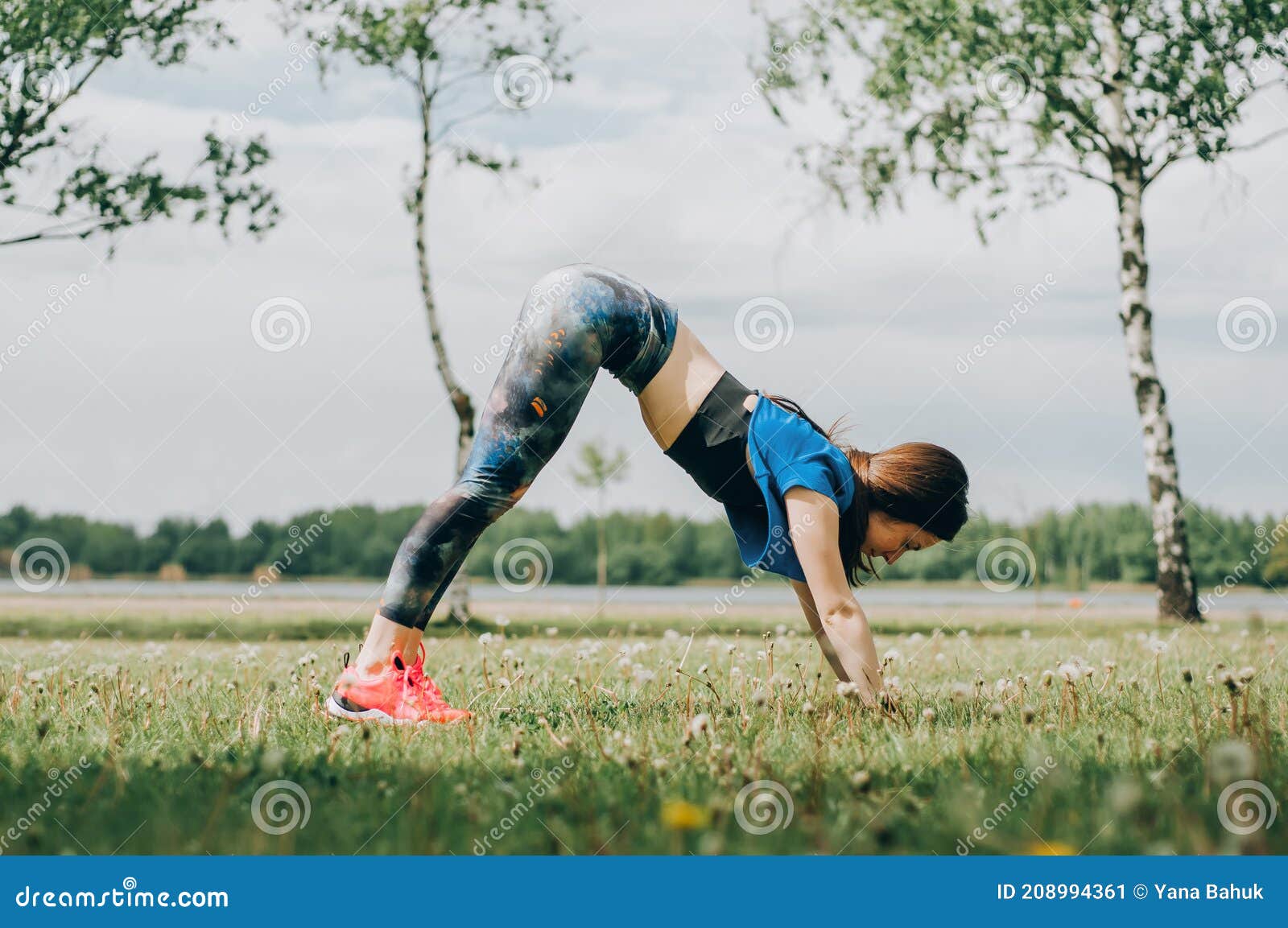 young brunette woman with bare feet  wearing black and purple fitness outfit  stretching on violet yoga mat outside on wooden pier