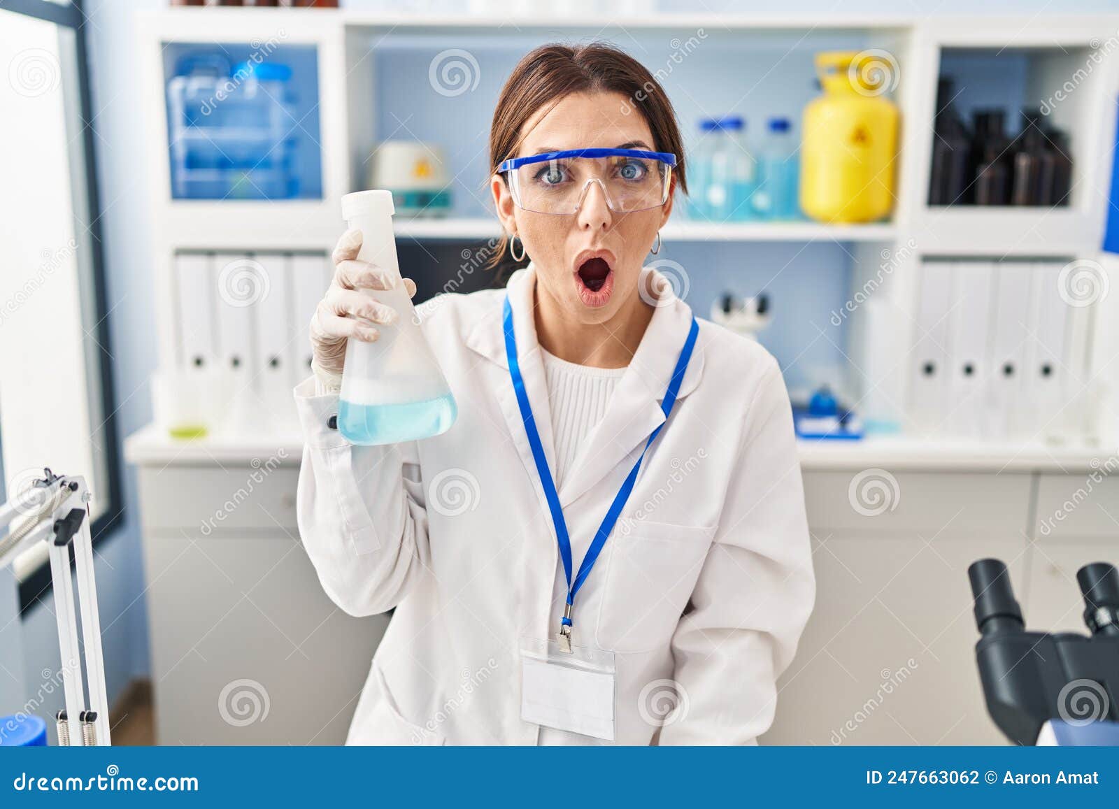 Young Brunette Woman Working at Scientist Laboratory Scared and Amazed ...