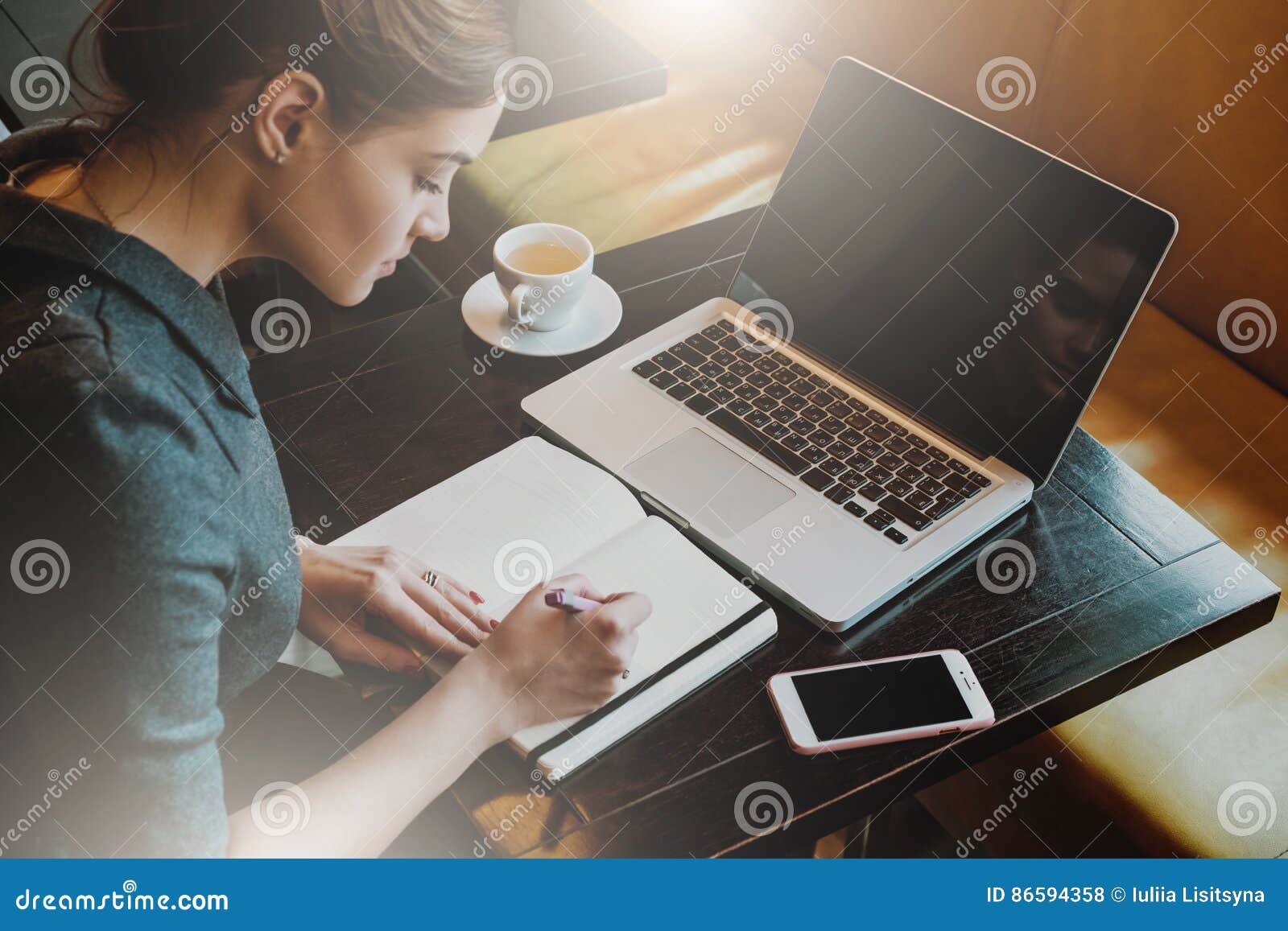 young business woman in gray dress sitting at table in cafe and writing in notebook.