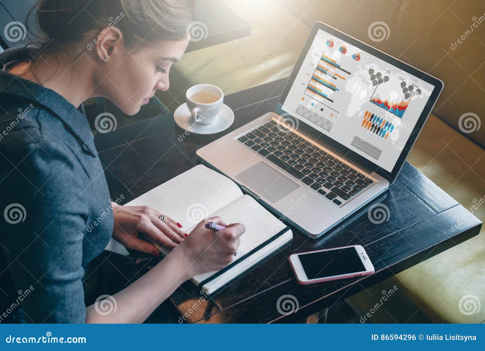 young business woman sitting at table and taking notes in notebook.on computer screen graphics and charts.