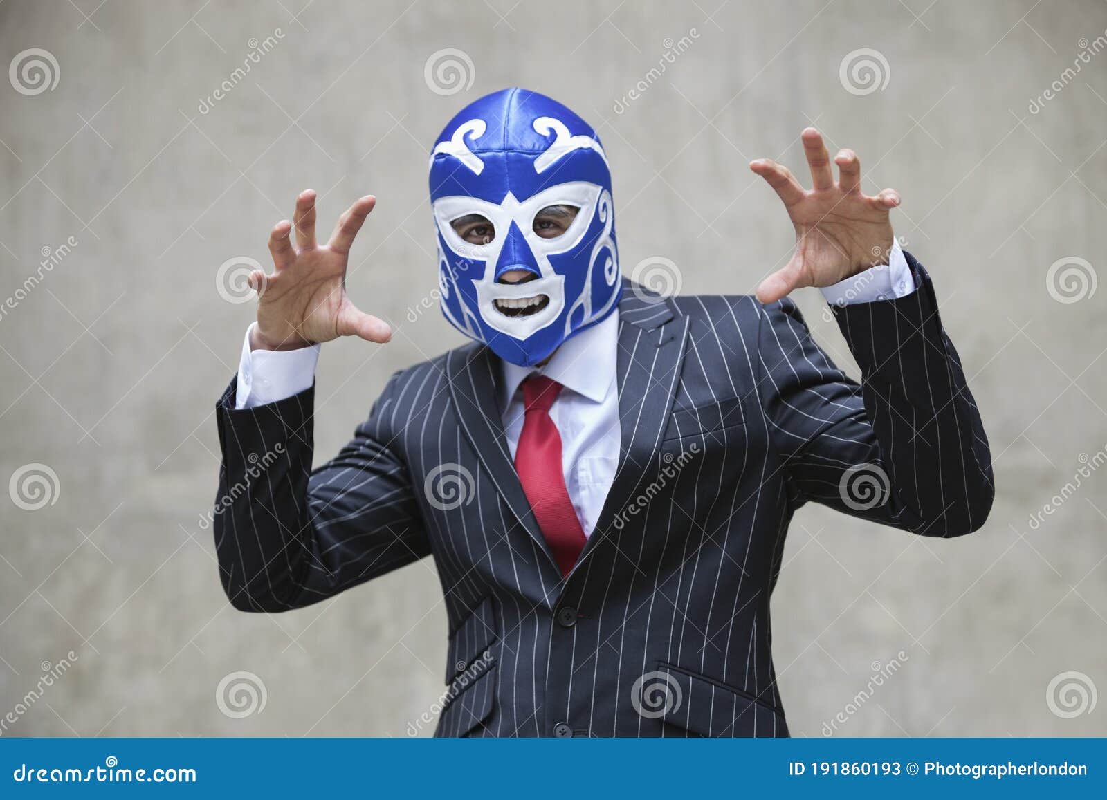 young businessman gesturing in wrestling mask and pinstripes suit over gray background