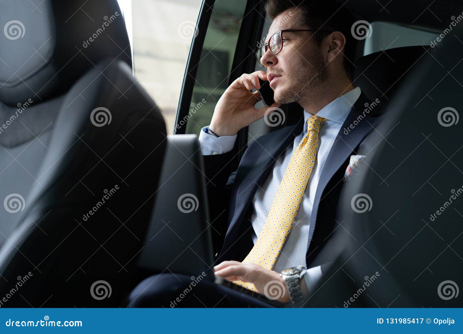 young businessman sitting on back seat of the car, while his chauffeur is driving automobile.
