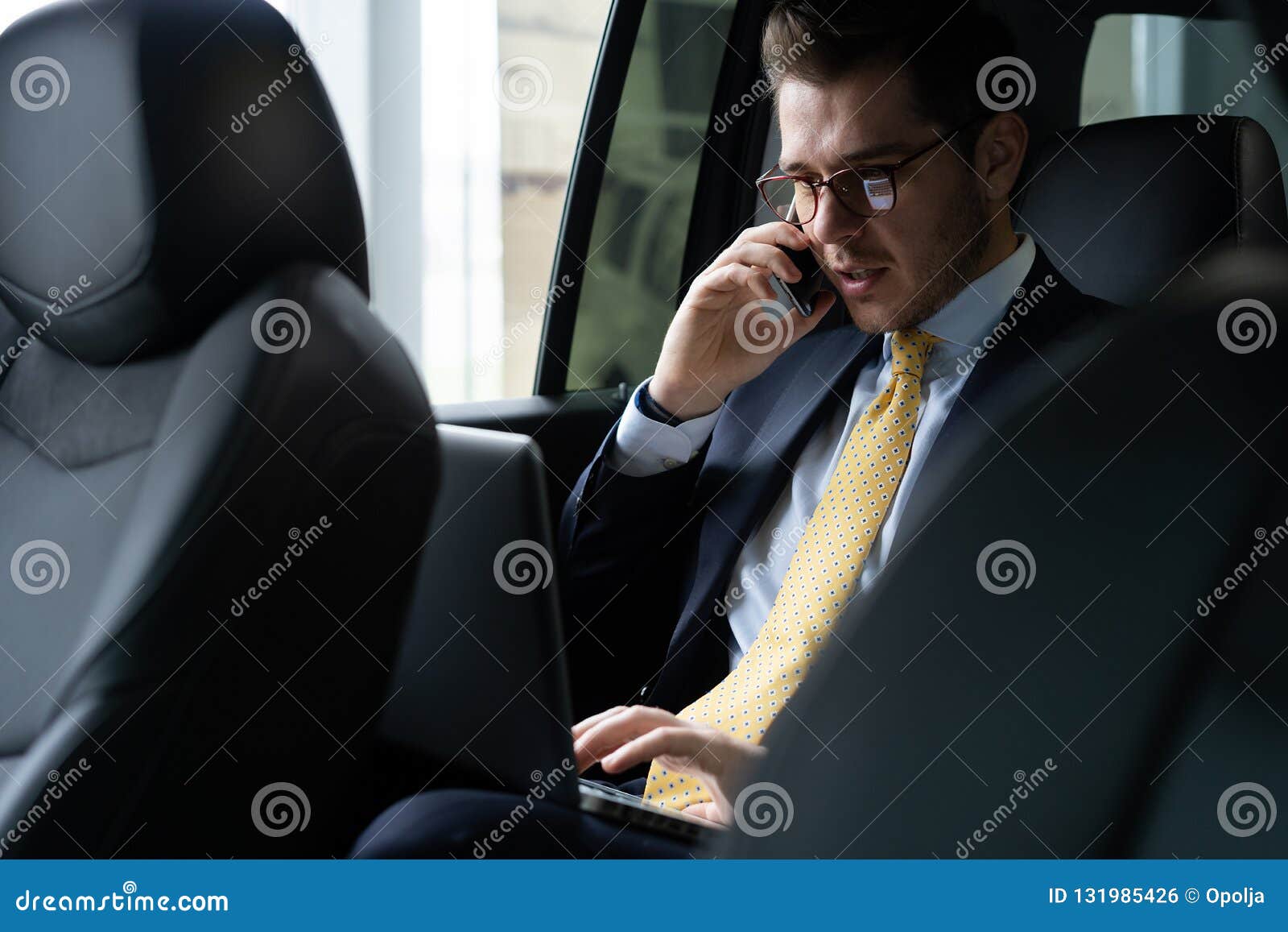 young businessman sitting on back seat of the car, while his chauffeur is driving automobile.