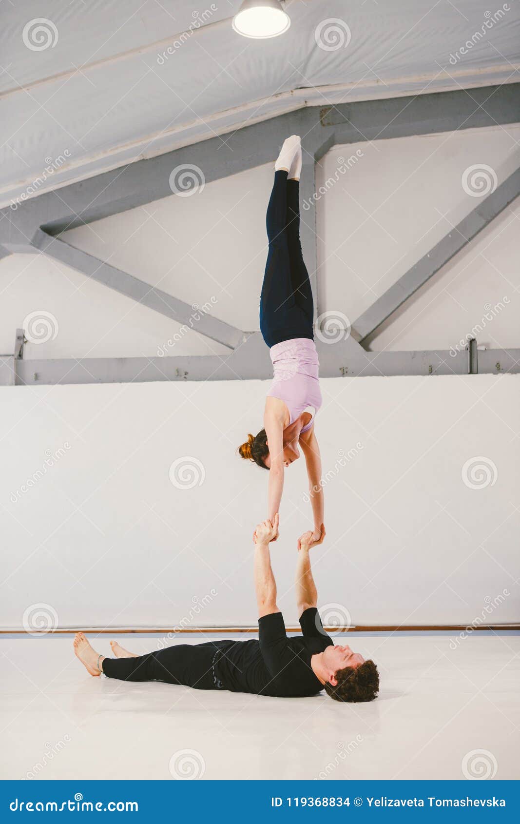 young caucasian male female couple practicing acrobatic yoga white gym mats loy hand to hand skills wind mill posit 119368834