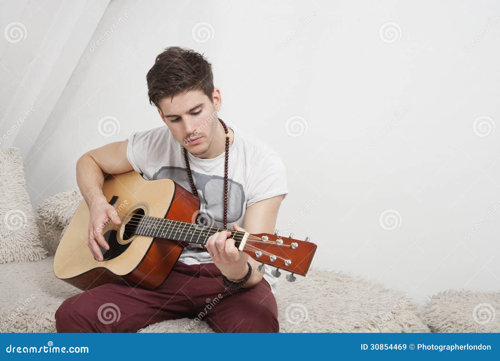 Young Caucasian Man Playing Guitar while Sitting on Fur Sofa Stock