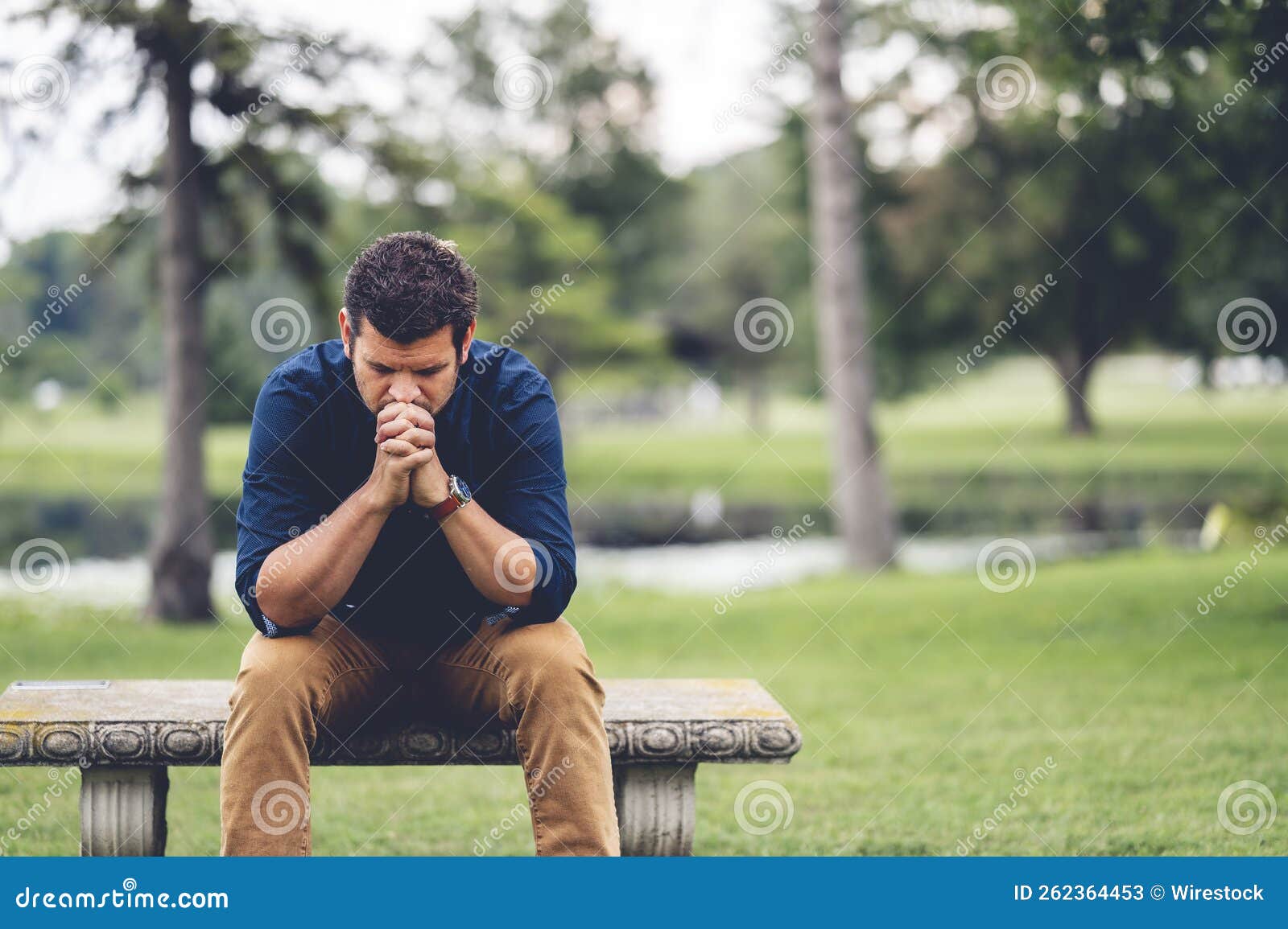 Young Caucasian Man Praying while Sitting on a Bench Stock Image