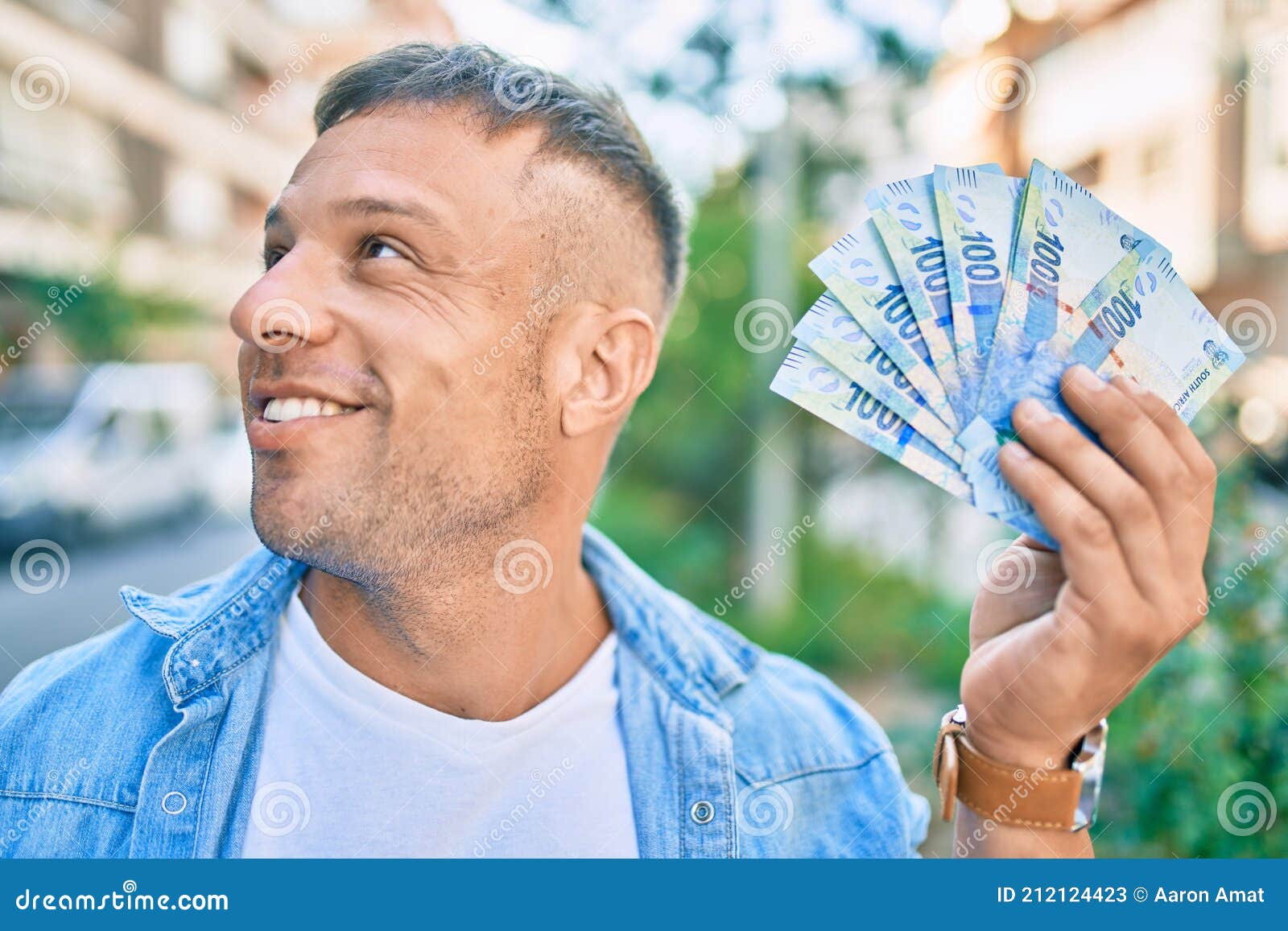 young caucasian man smiling happy holding south african rands banknotes standing at the city