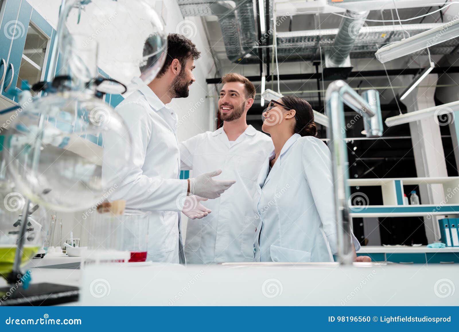 Young Chemists in White Coats Standing and Talking in Laboratory Stock