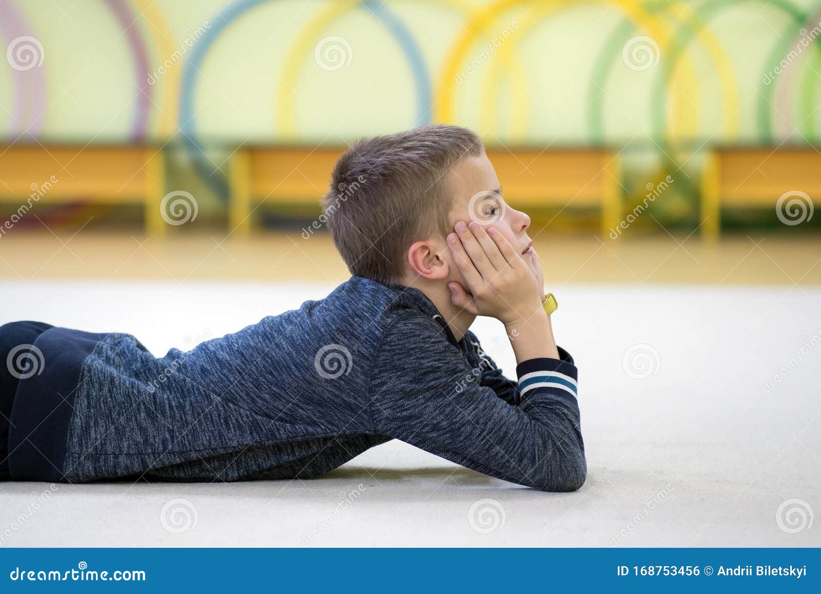 Young Child Boy Laying Down And Relaxiong While Resting On The Floor Inside Sports Room In A