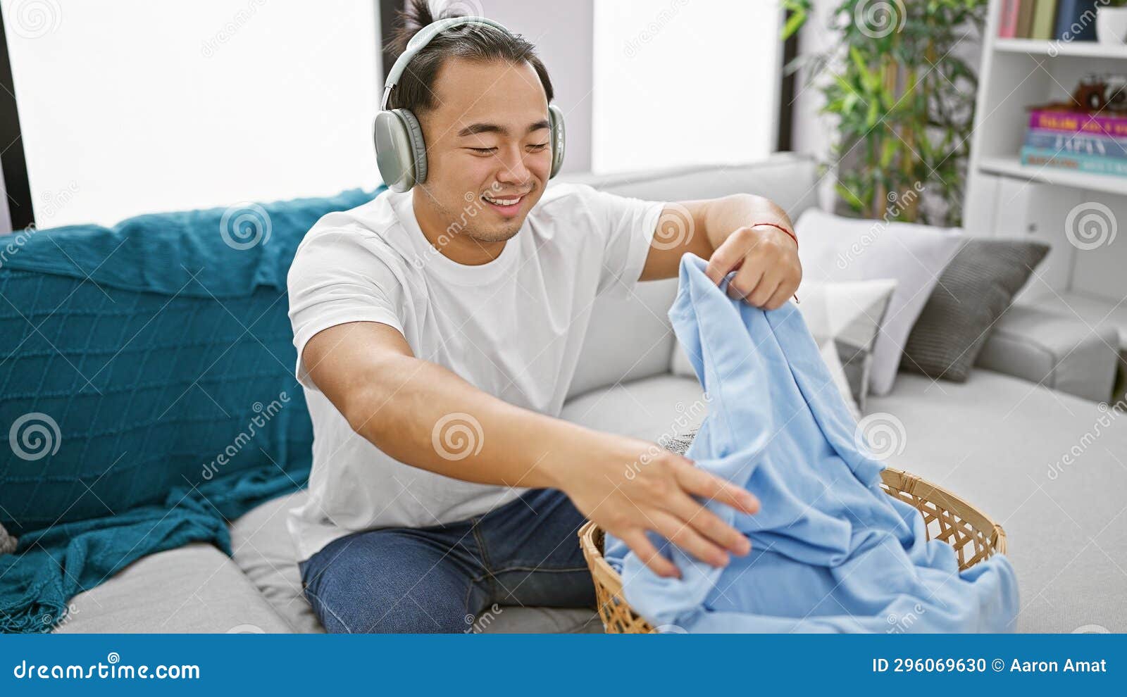 young chinese guy indulging in music while smilingly doing laundry chores at home