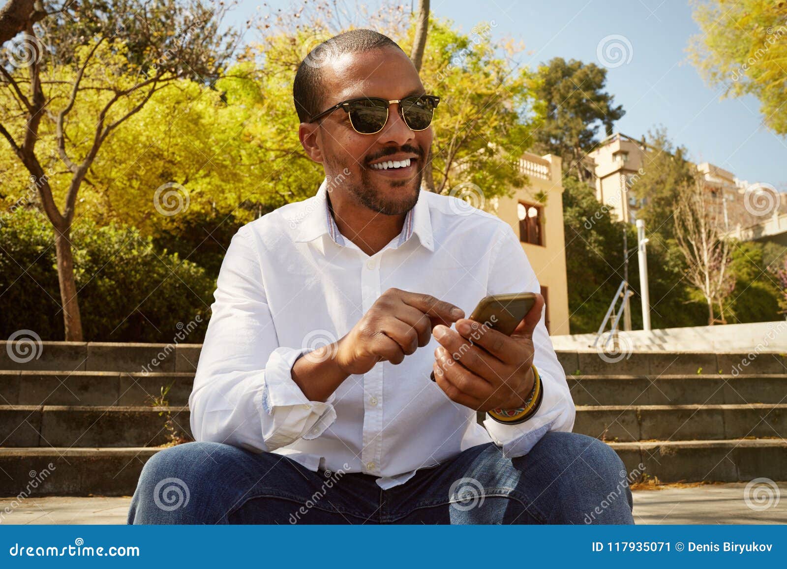 young confident african man pointing hand on smartphone while sitting at sunny city park.concept of happy business