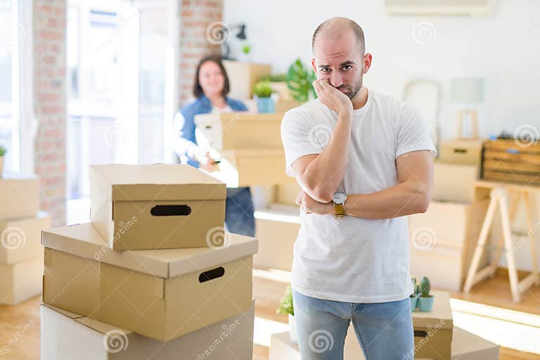 young-couple-arround-cardboard-boxes-moving-to-a-new-house-bald-man-standing-at-home-thinking