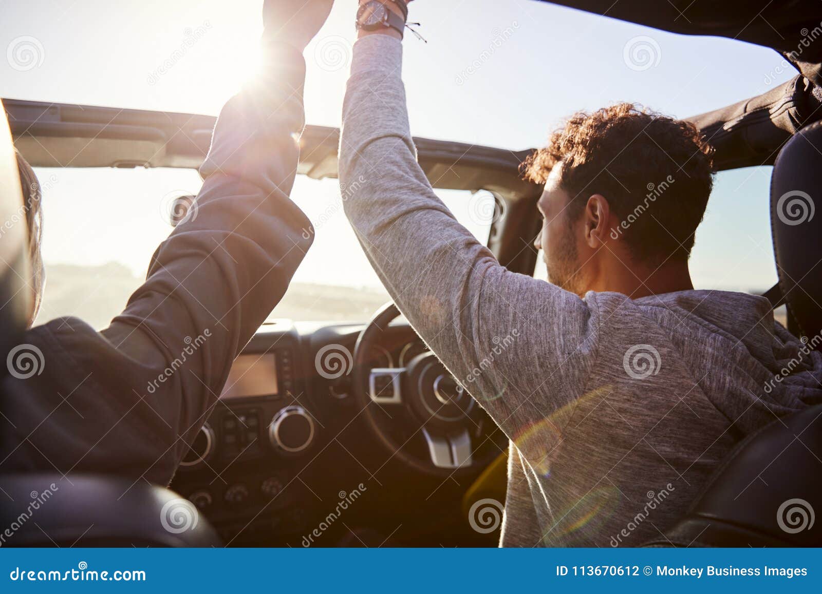 young couple driving with sunroof open and hands in the air