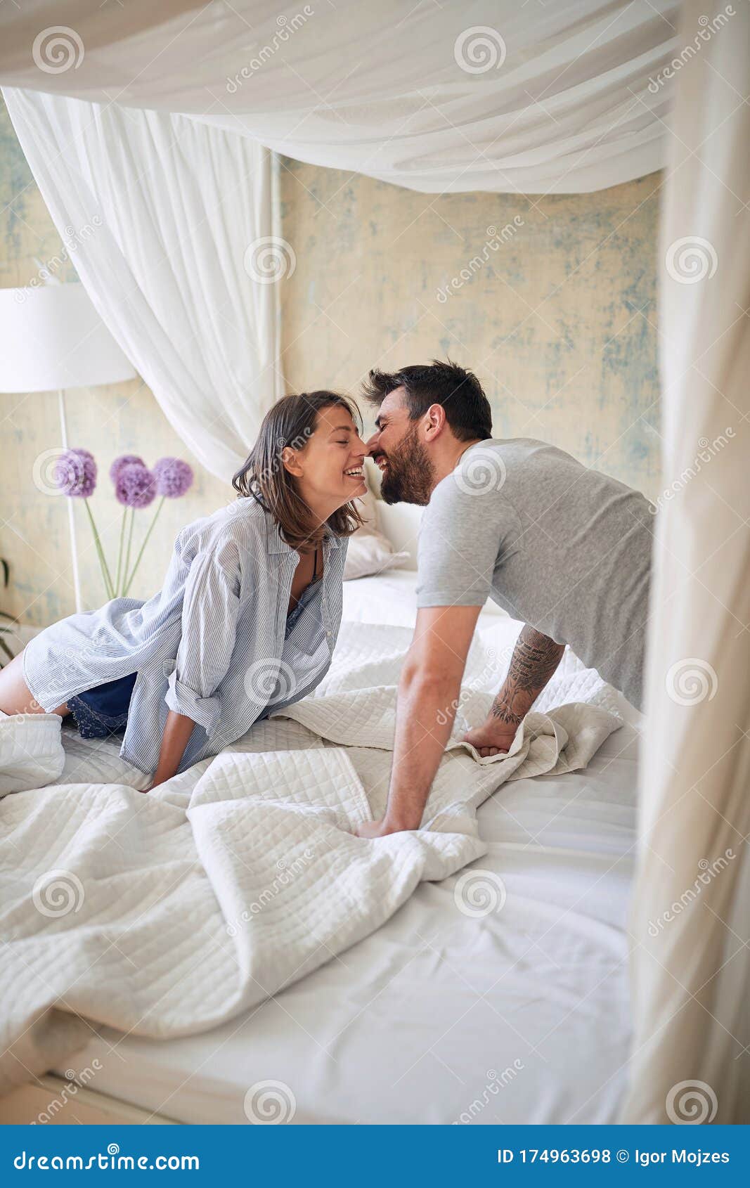 Young Couple Kissing In The Bedroom While Making Bed In The Morning