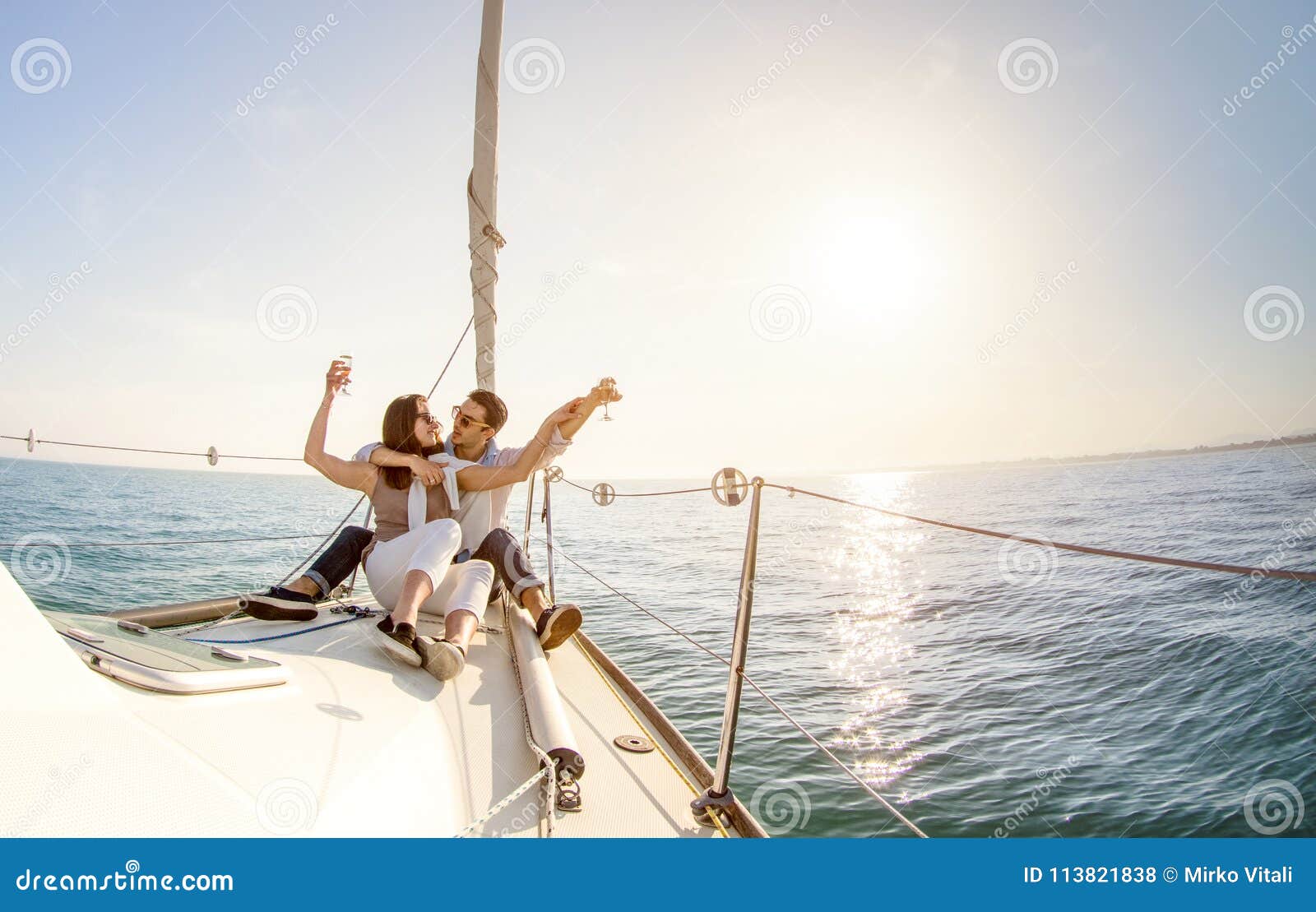 young couple in love on sail boat with champagne at sunset - hap