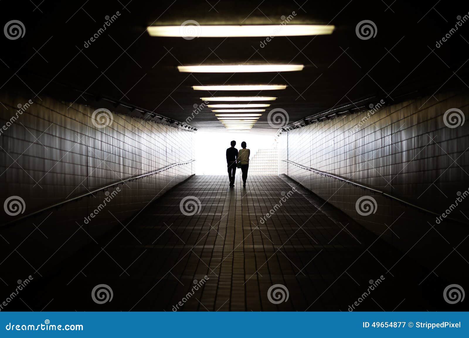 young couple in silhouette walking towards exit of pedestrian underpass