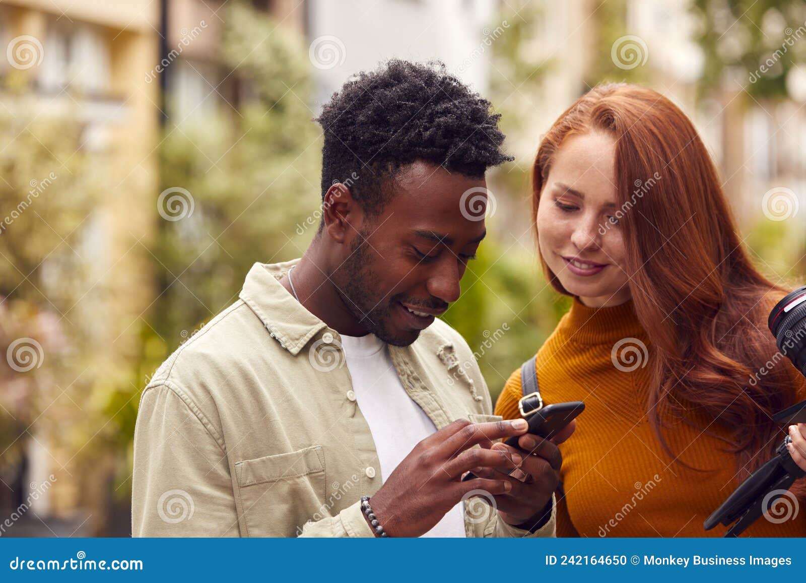 young couple travelling through city together vlogging with camera looking at mobile phone