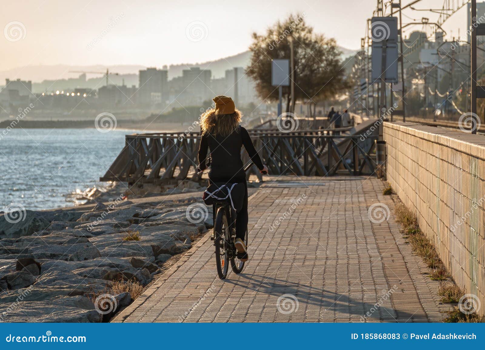 young curly girl in a yellow hat rides a bicycle at sunset on the promenade road of maresme, catalonia, spain