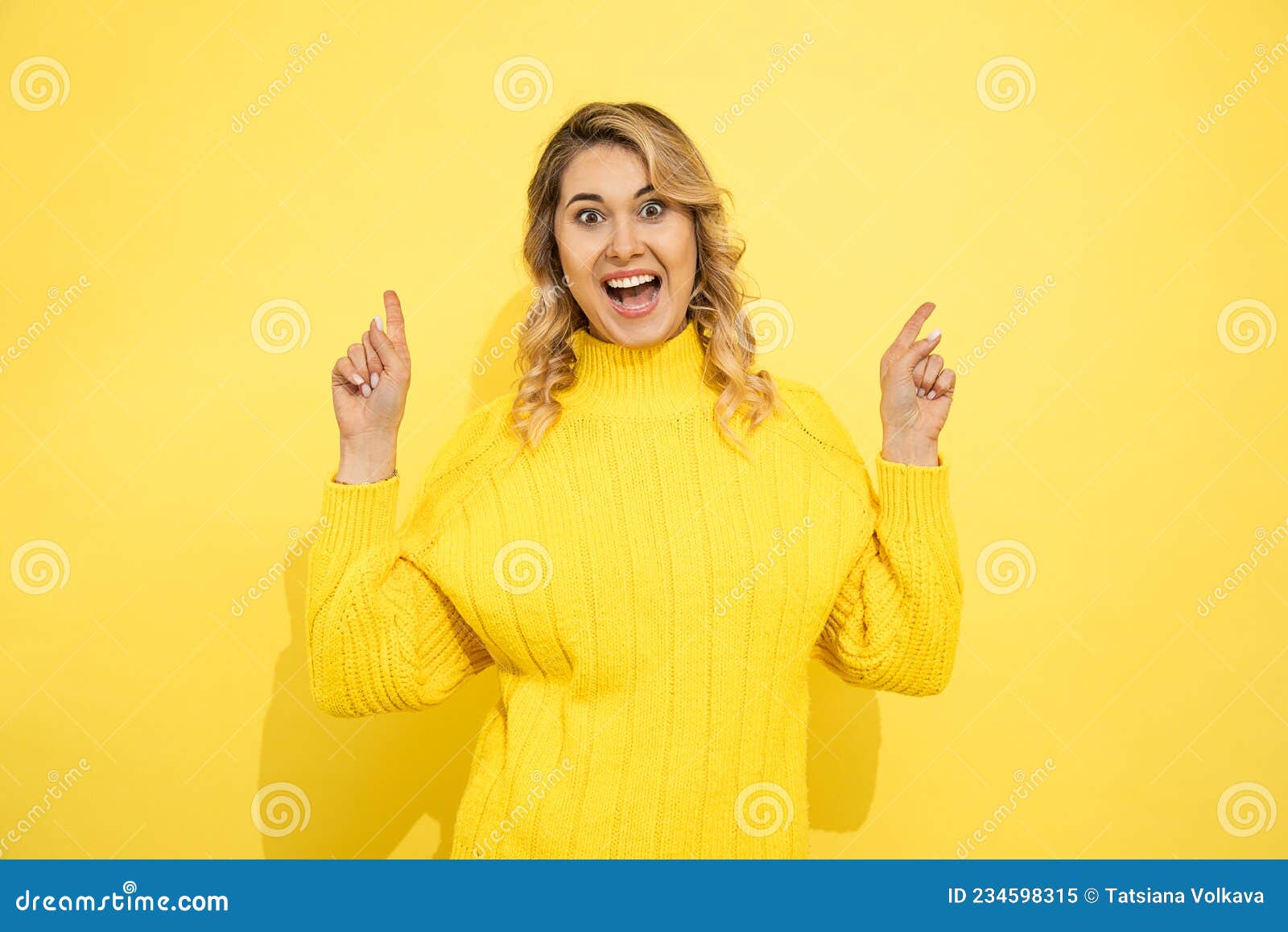 young cute beautiful happy smiling woman wearing yellow sweater standing over yellow  background, pointing with hands to