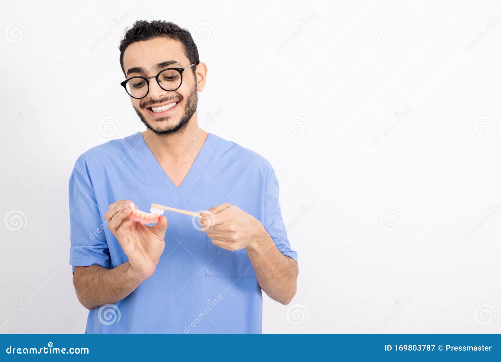 Young Dentist in Uniform Brushing False Teeth with Toothbrush in