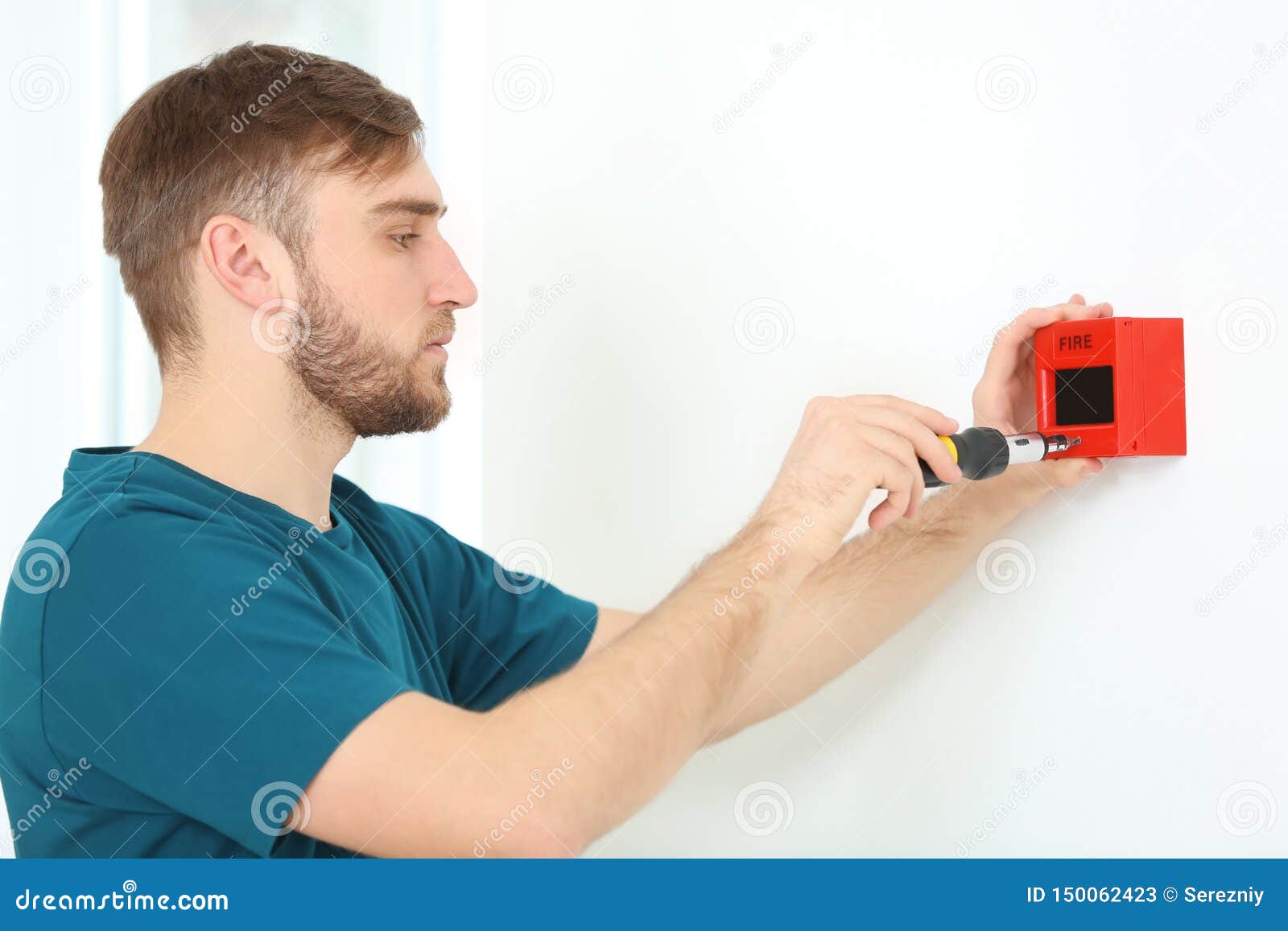 Young Electrician Installing Fire Alarm Unit on Wall Stock Image