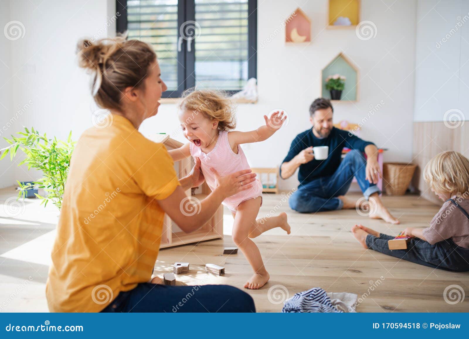 young family with two small children indoors in bedroom playing.