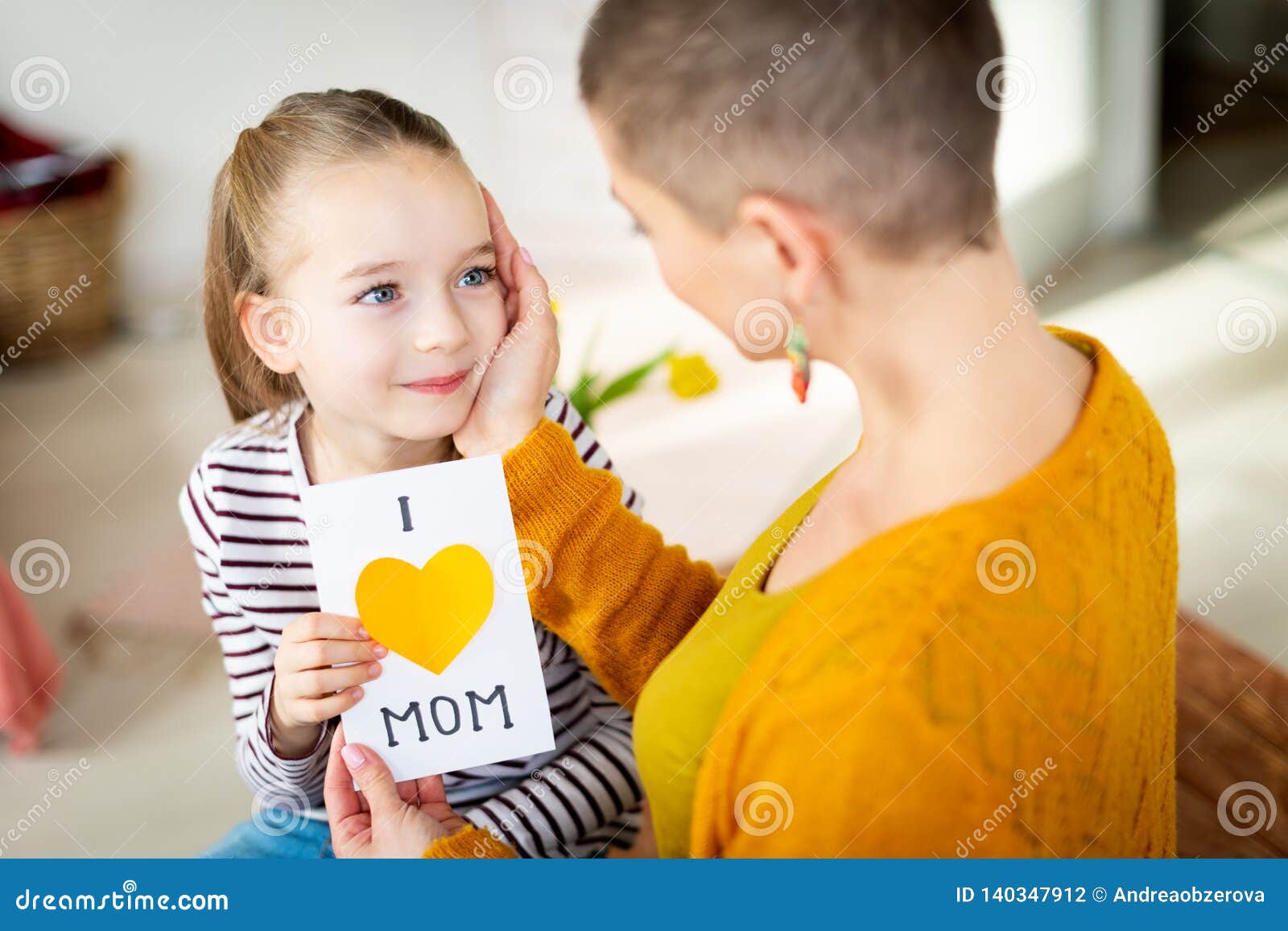 young female cancer patient thanking her adorable young daughter for homemade i love mom greeting card. happy mother`s day .