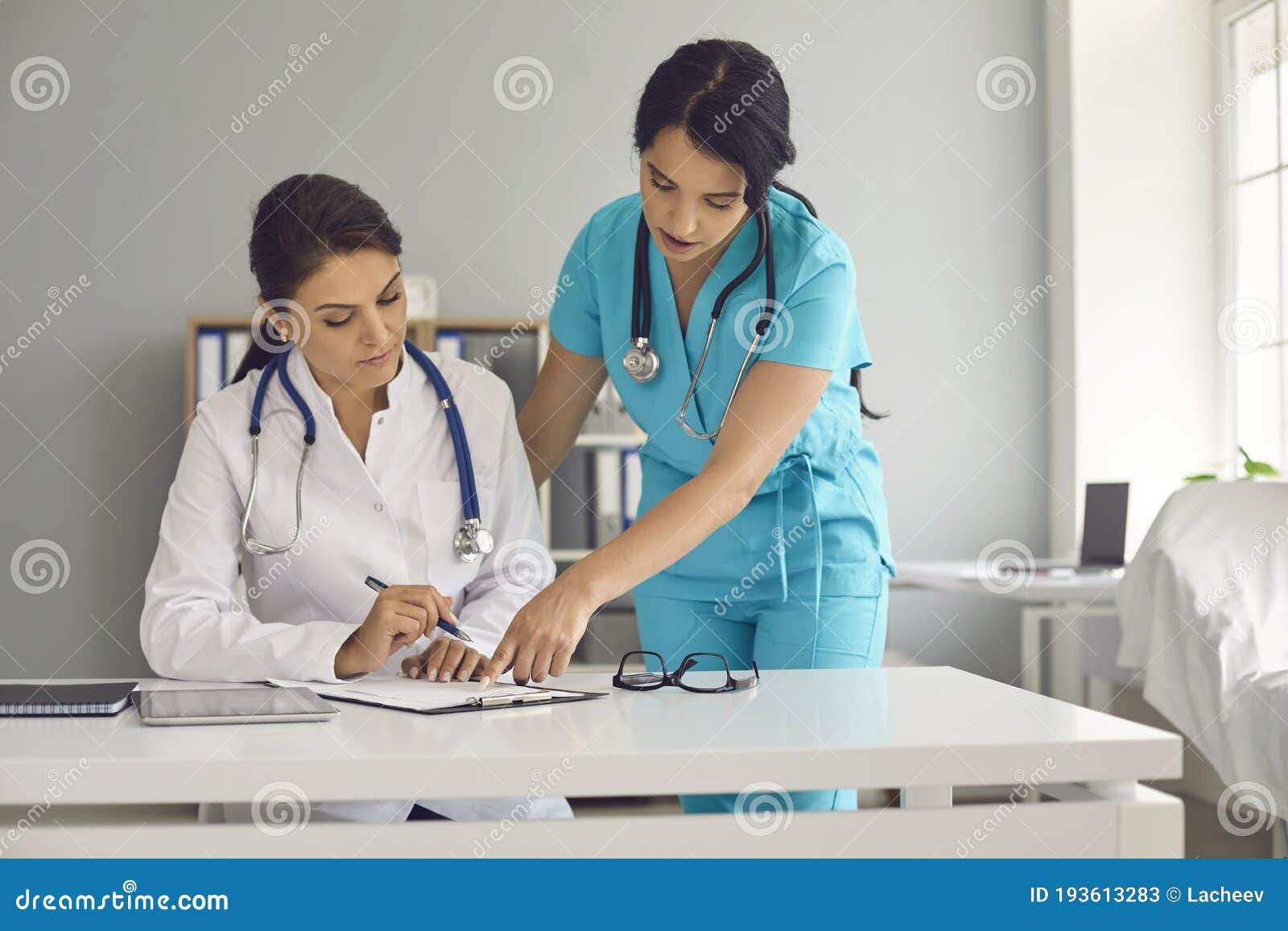 young female doctor and her assistant working together at hospital. physician and nurse with documents at medical office