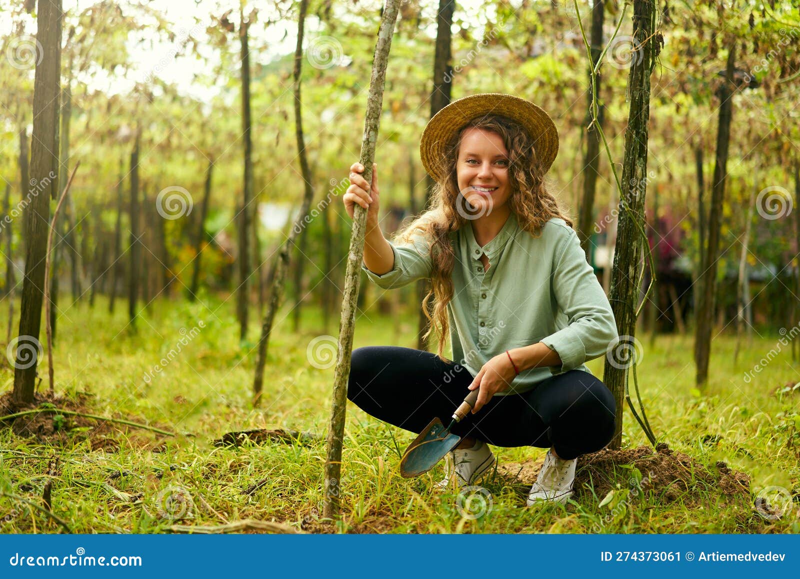 young female gardener smiles on her farm sitting with garden trowel in soil among plants. happy cauasian woman in her