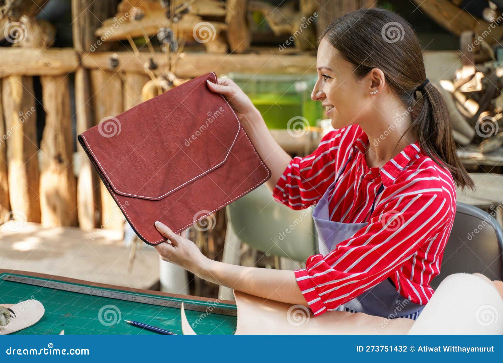 young female leather goods maker looking and check the neatness of the leathers bag before sell to customer in workshop