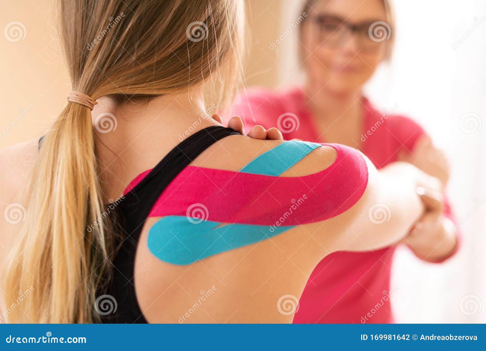 young female patient wearing kinesio tape on her shoulder exercising with a professional physical therapist. kinesiology.