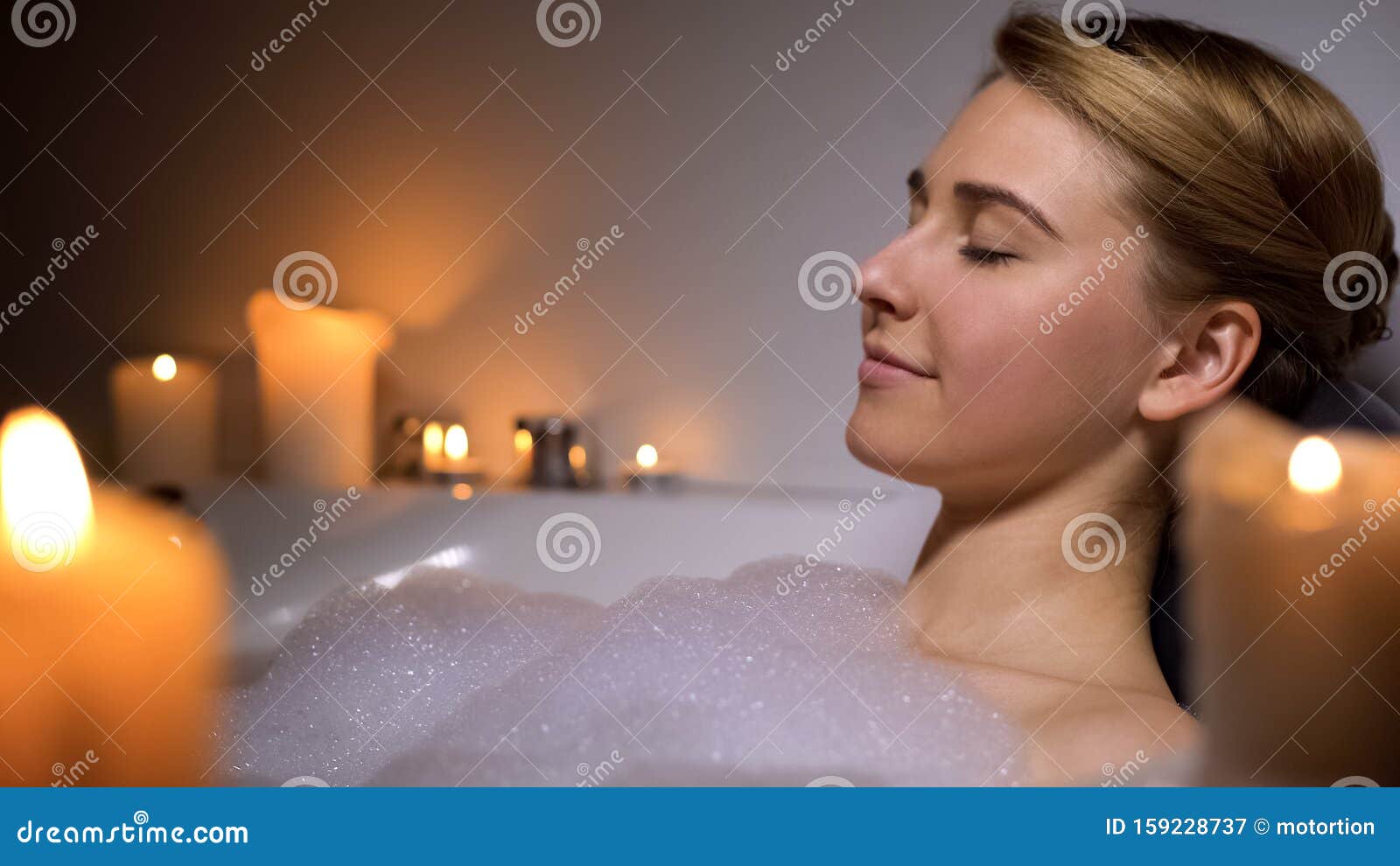 Young Female Relaxing In Warm Bath With Foam Bubbles And Candles