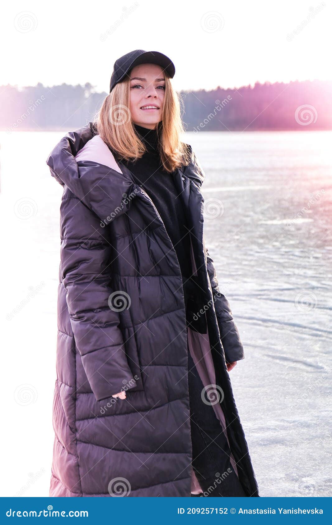 young female smiling and looking at a camera in a snow landscape. happy hipster girl with hip hop warm winter clothes. staying on