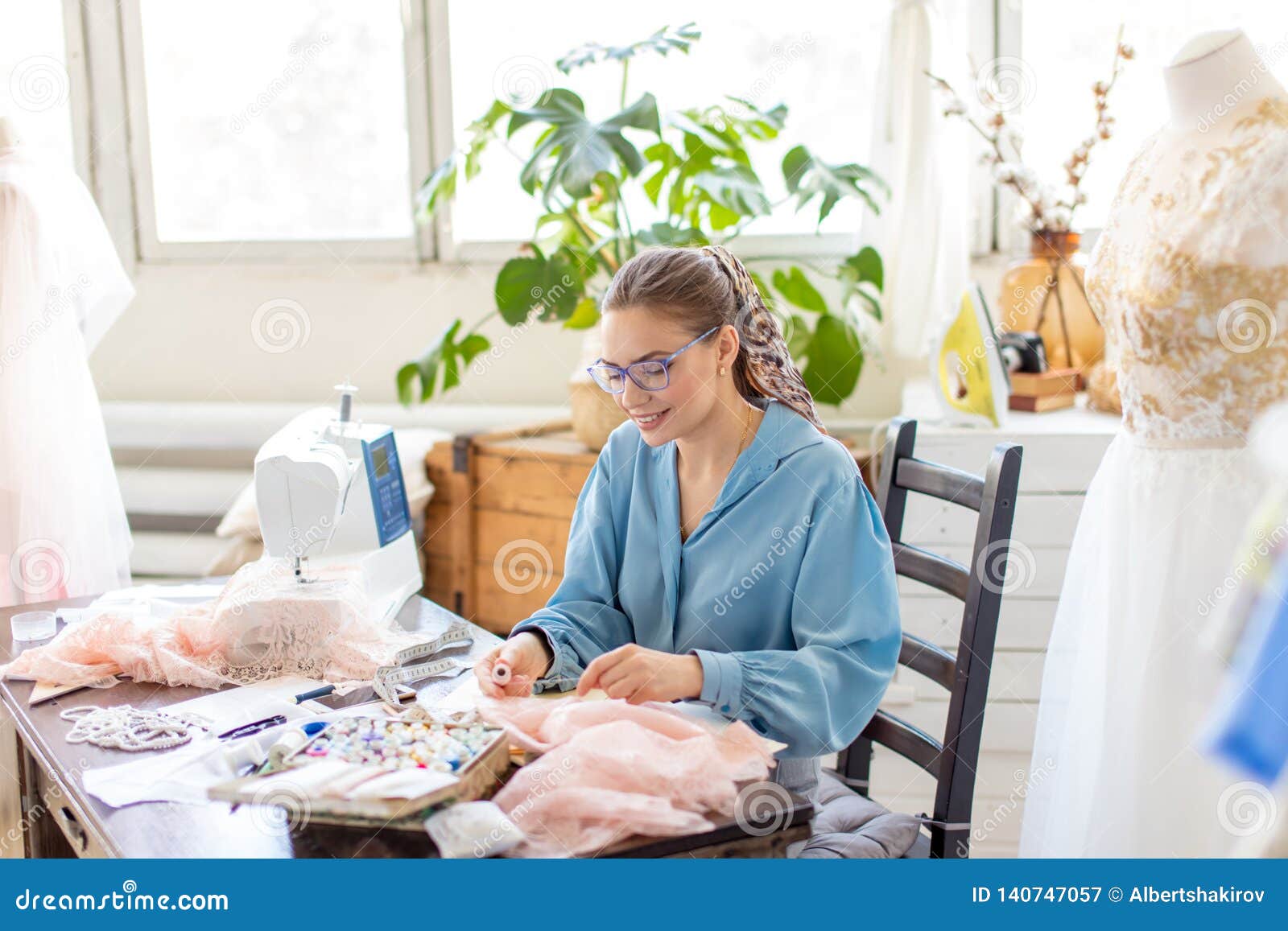 Young Female Tailor Sits at Workplace and Chooses Color of Threads in