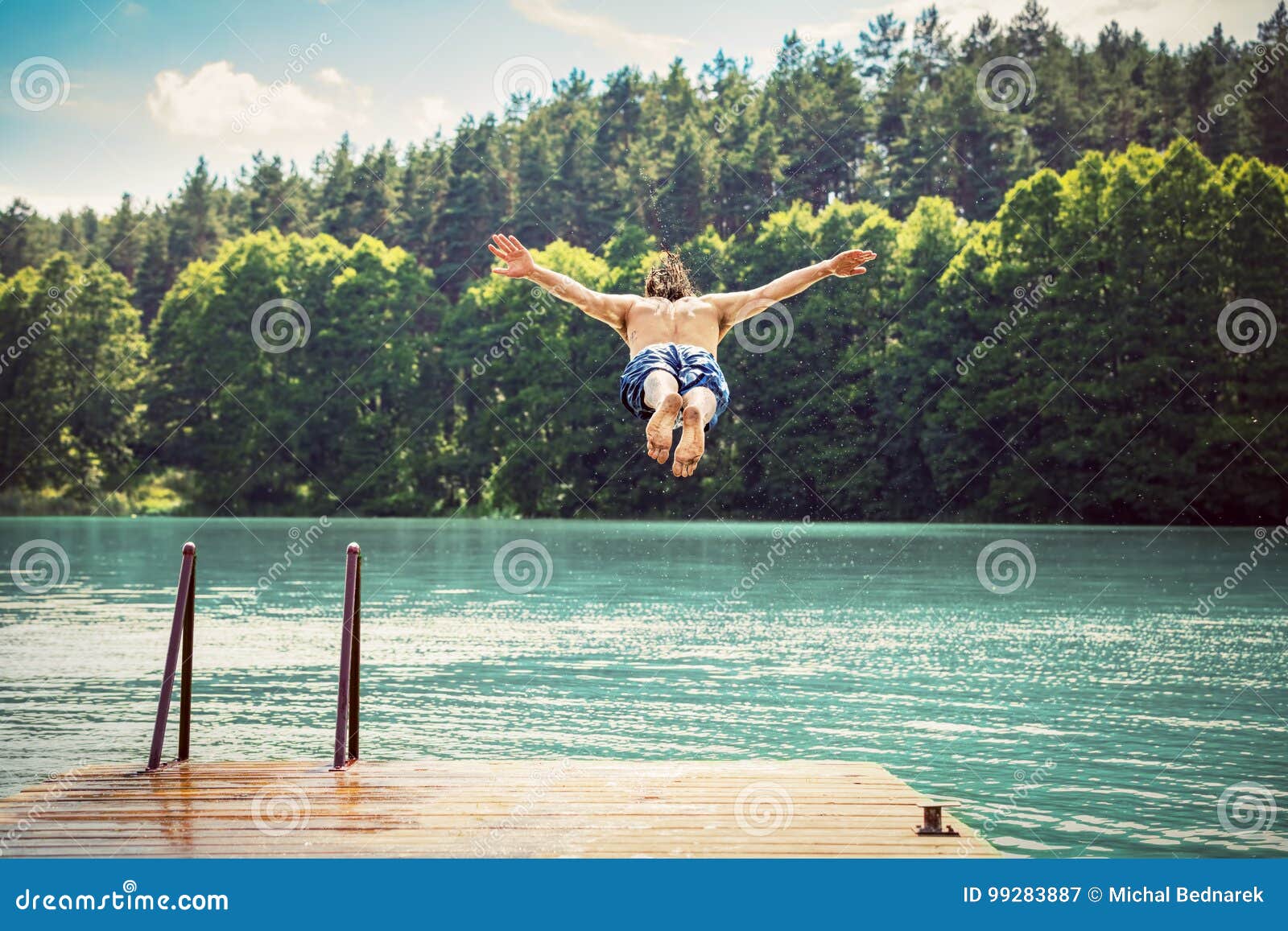 young fit man making a jump into a lake.