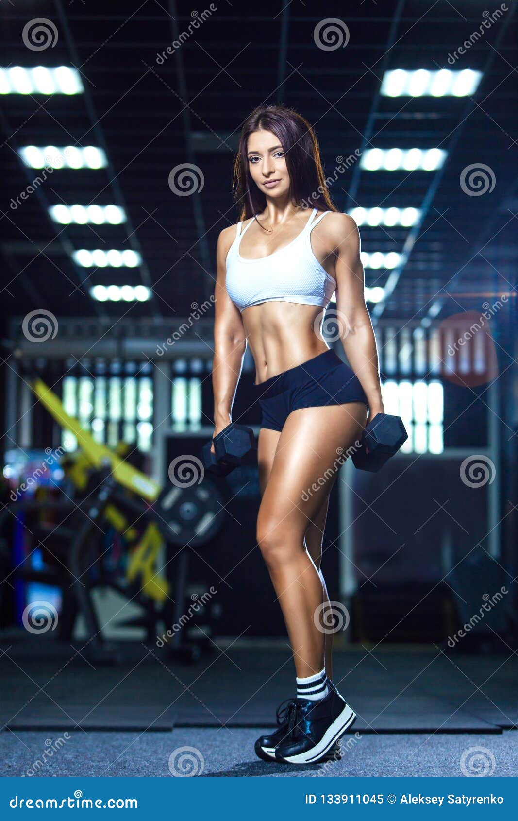 Young beautiful girl with big breasts and good figure in sports hall with  dumbbells in hands Stock Photo