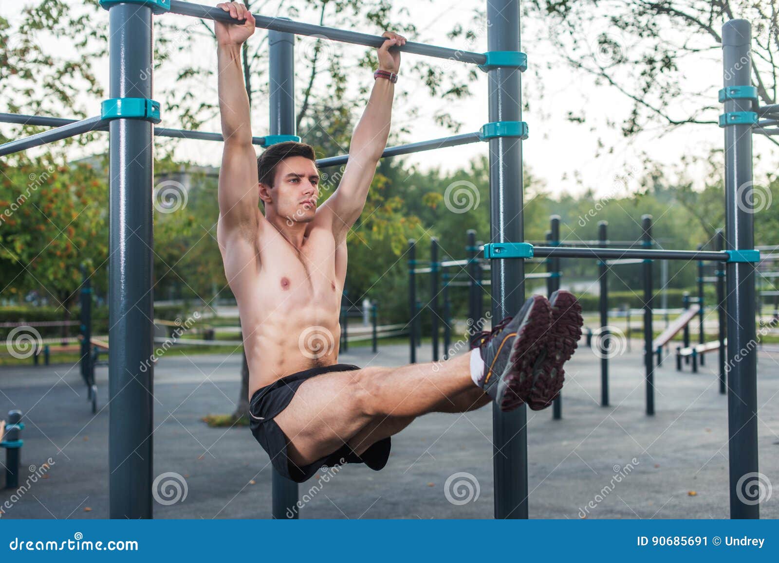 young fitness man doing hanging leg raises exercise working out his abs in the park.