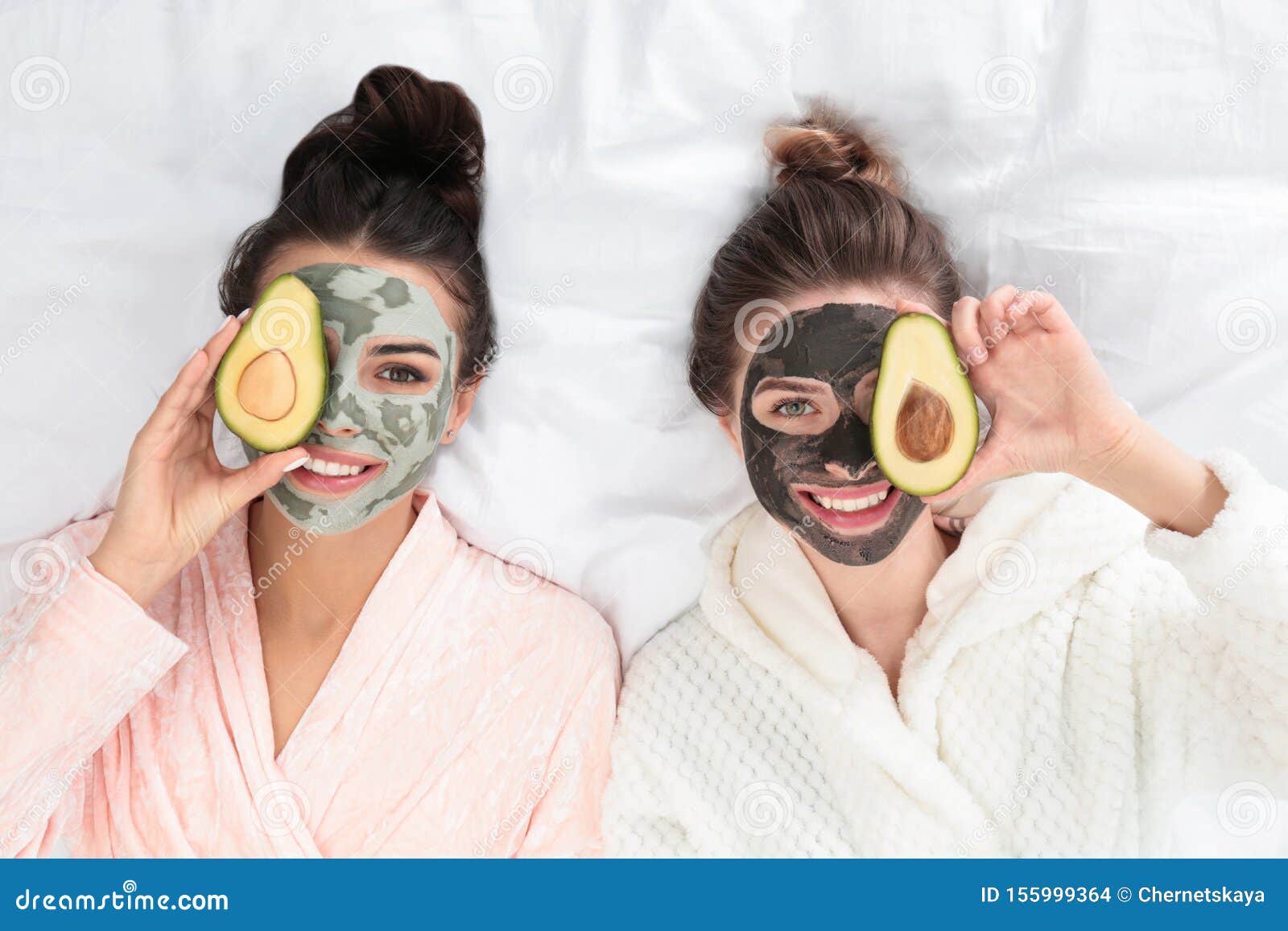 young friends with facial masks  fun on bed at pamper party, top view