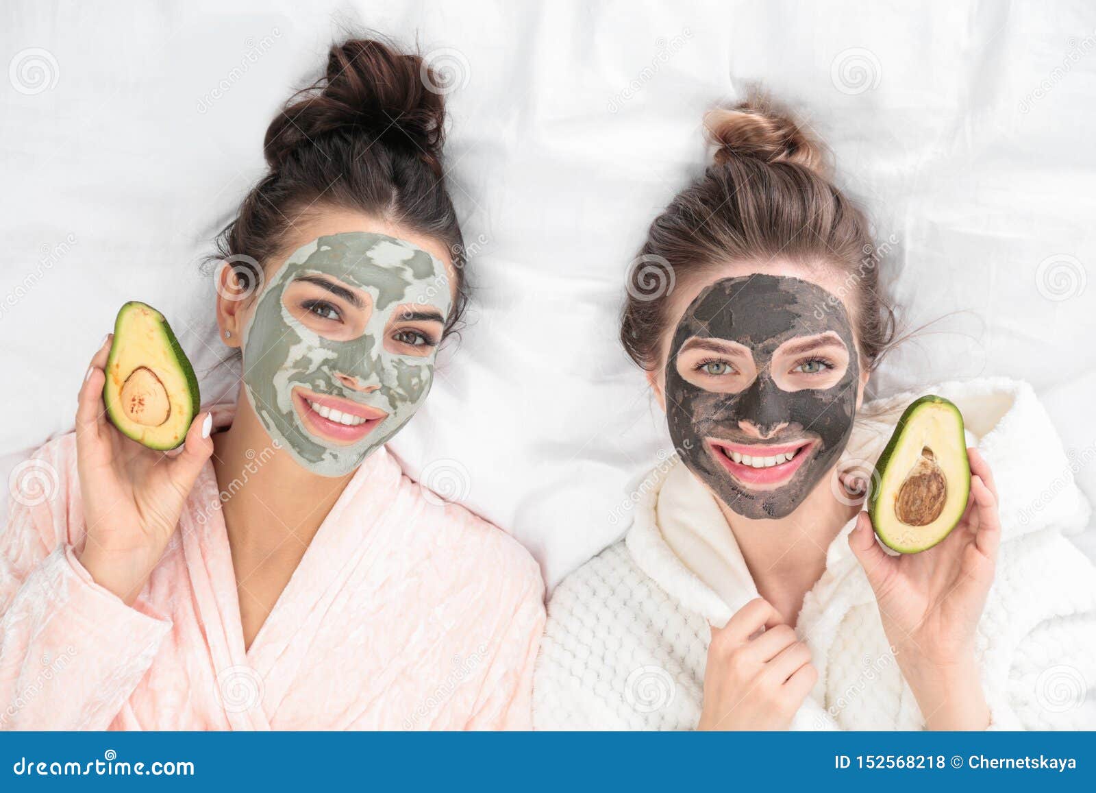 young friends with facial masks having fun on bed at pamper party