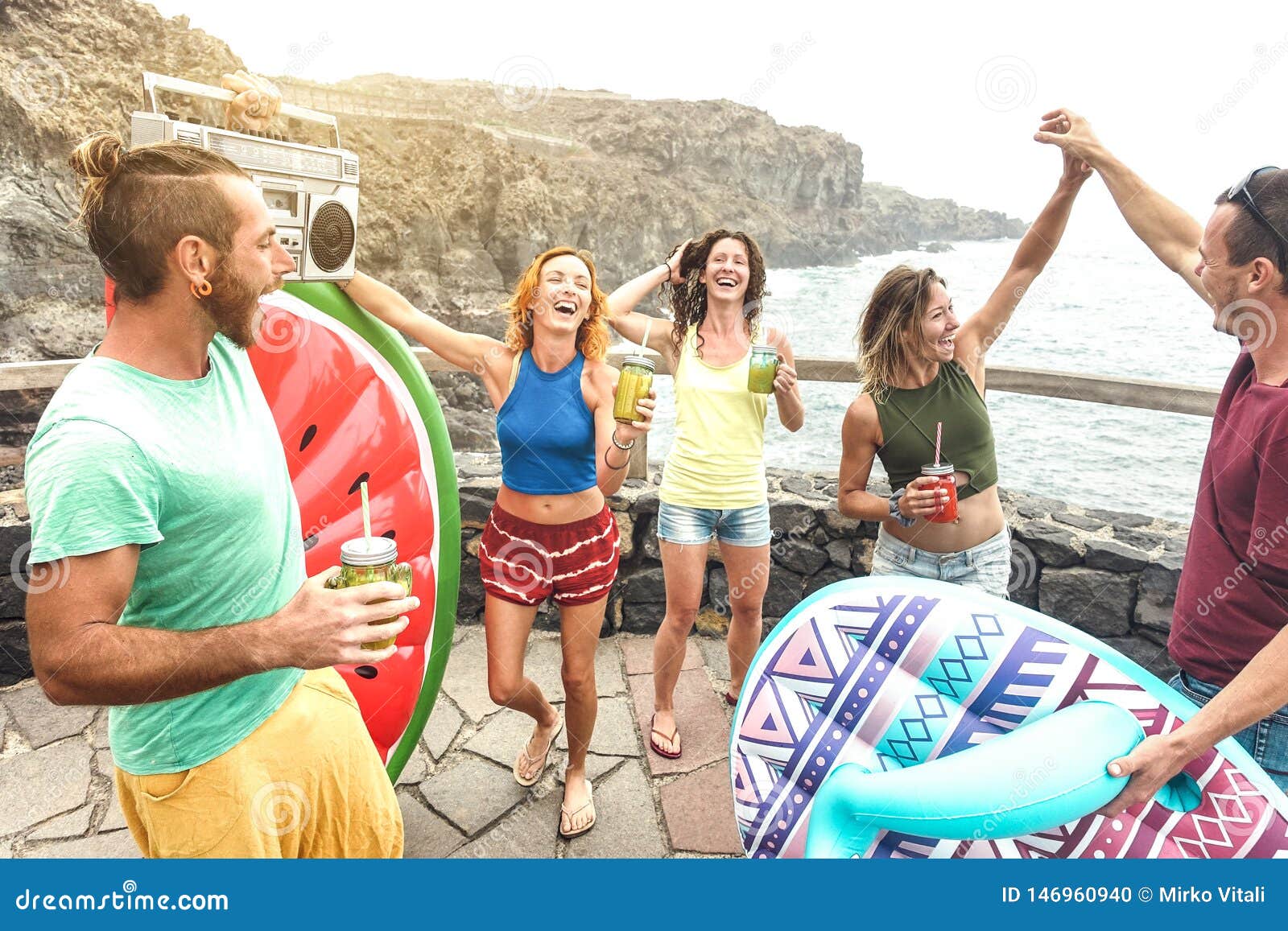 young friends vacationer having fun at natural pool on travel location - happy millenial people dancing and drinking cocktails