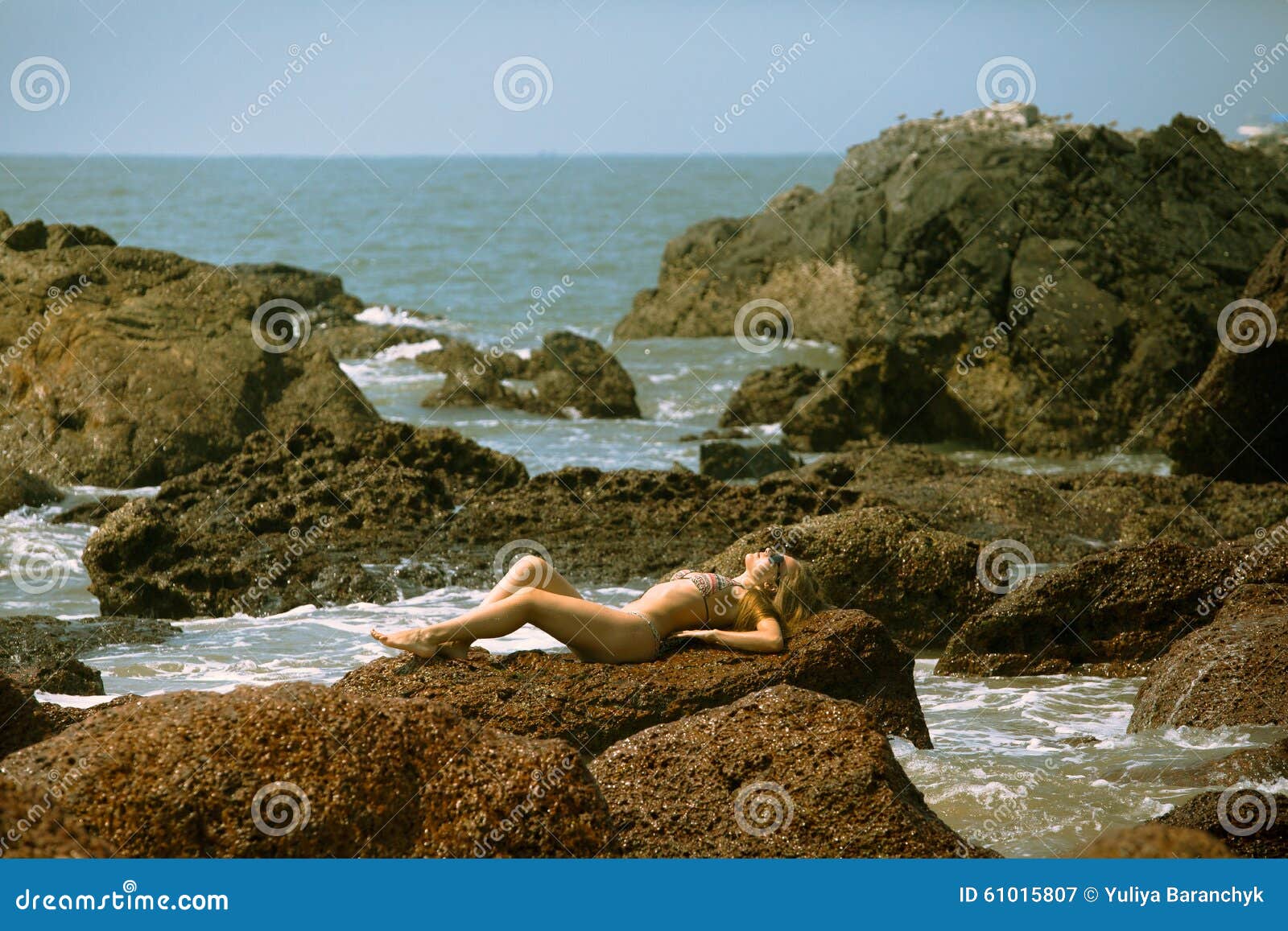 young girl in bikini with beutiful body and sunglasses lying on the stones on the beach