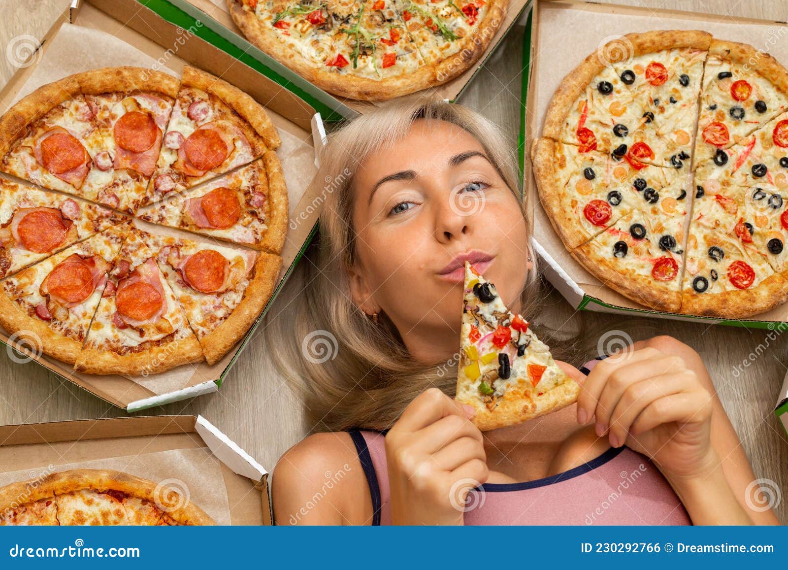 A Young Girl With Blond Hair In A Pink Tank Top Is Holding A Slice Of 