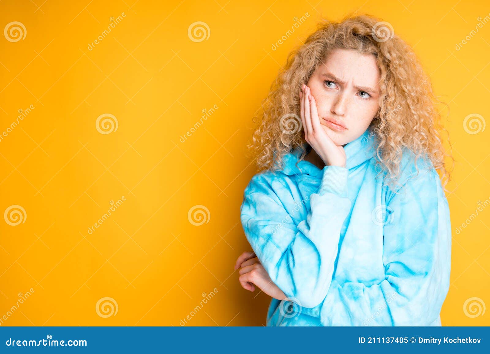 a young girl in a blue sweater stands against a bright background showing sadness. emotions