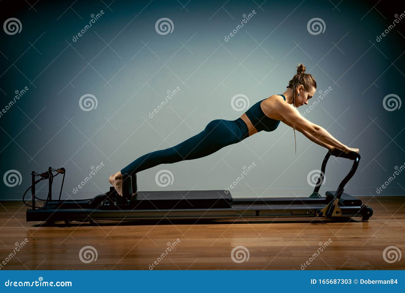 young girl doing pilates exercises with a reformer bed. beautiful slim fitness trainer on reformer gray background, low