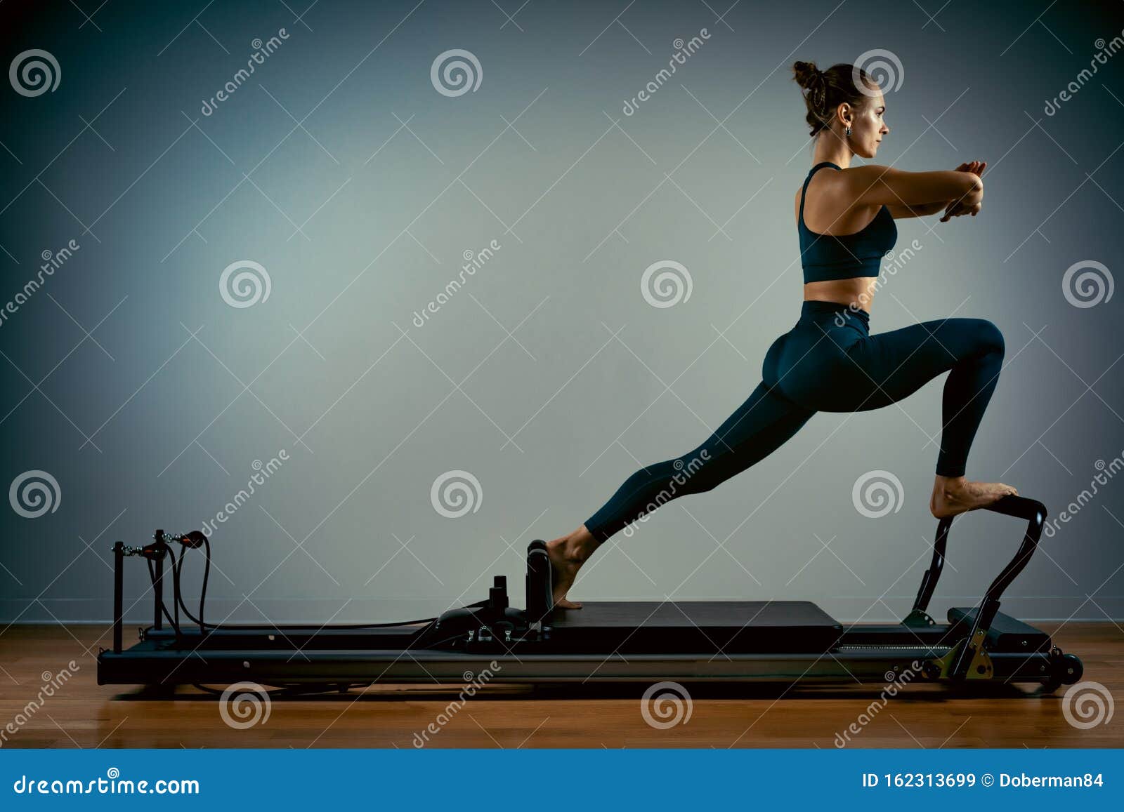 young girl doing pilates exercises with a reformer bed. beautiful slim fitness trainer on a reformer gray background