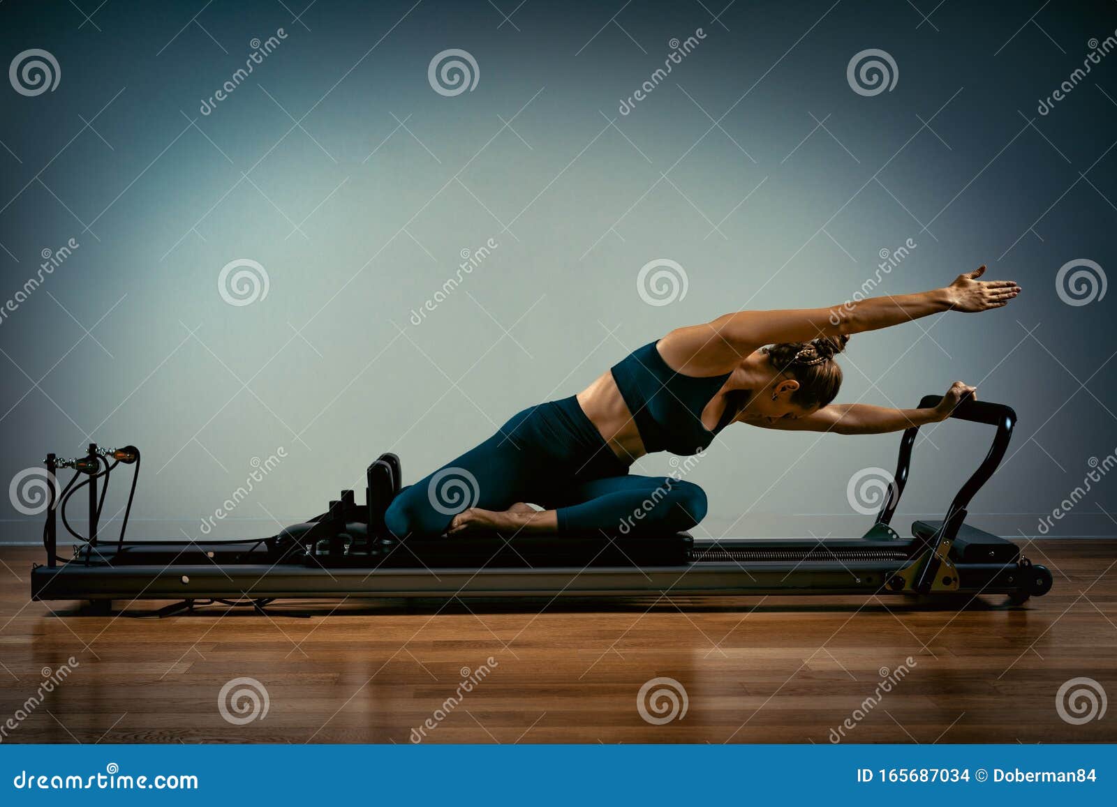 young girl doing pilates exercises with a reformer bed. beautiful slim fitness trainer on reformer gray background, low