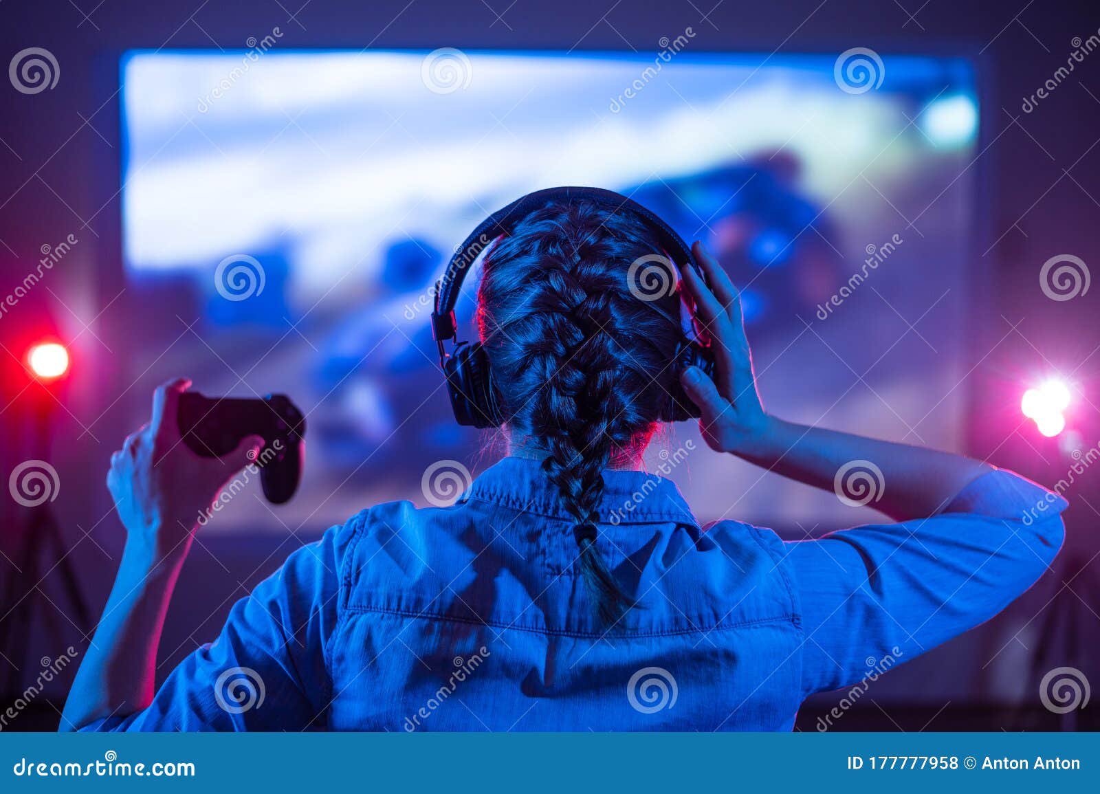 Girl in headphones plays a video game on the big TV screen. Gamer with a  joystick.