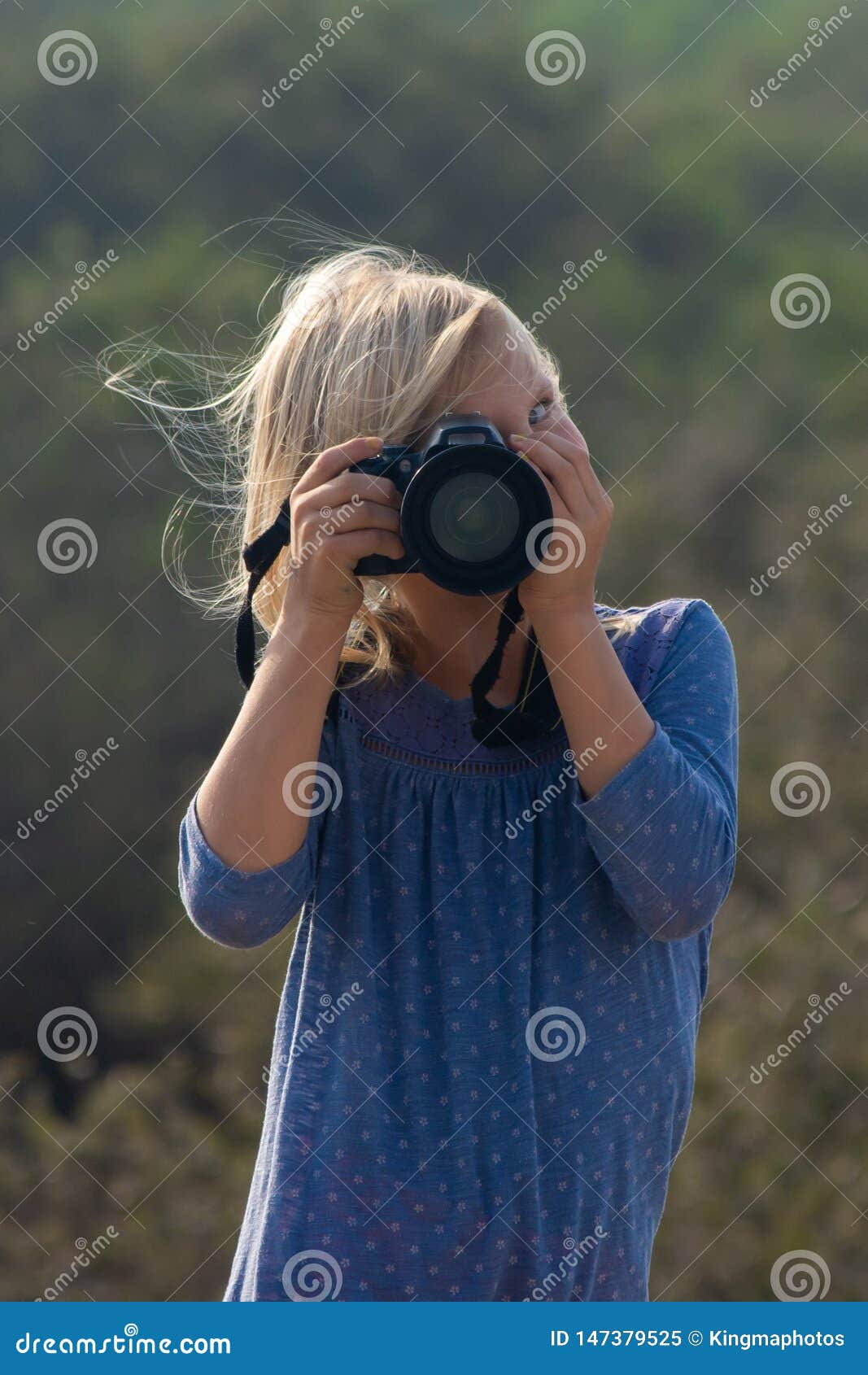 young girl in nature taking pictures with a large dslr and a zoon lens